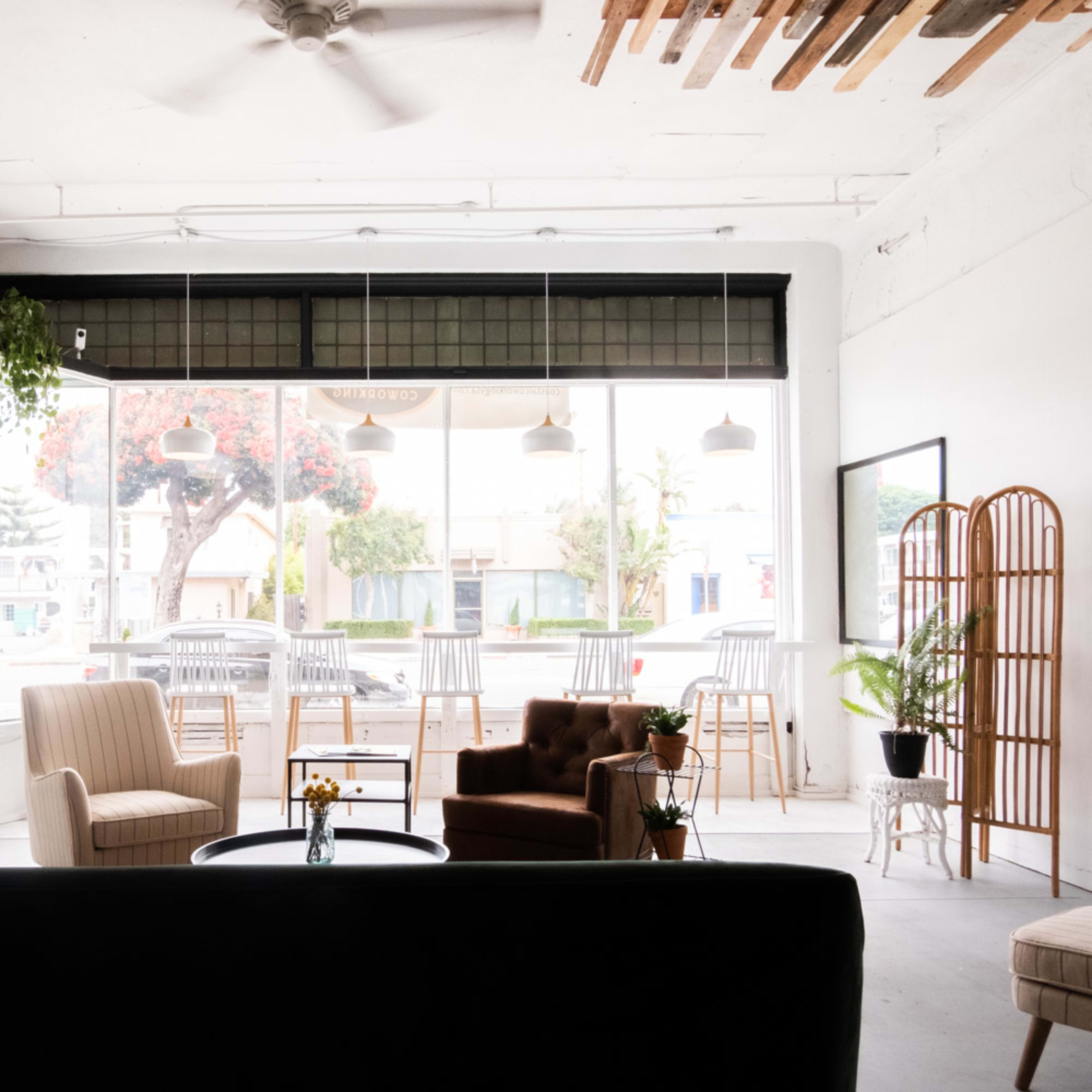 A spacious, open room with large windows, featuring a seating area with two armchairs, a coffee table, and a view of outdoor seating.