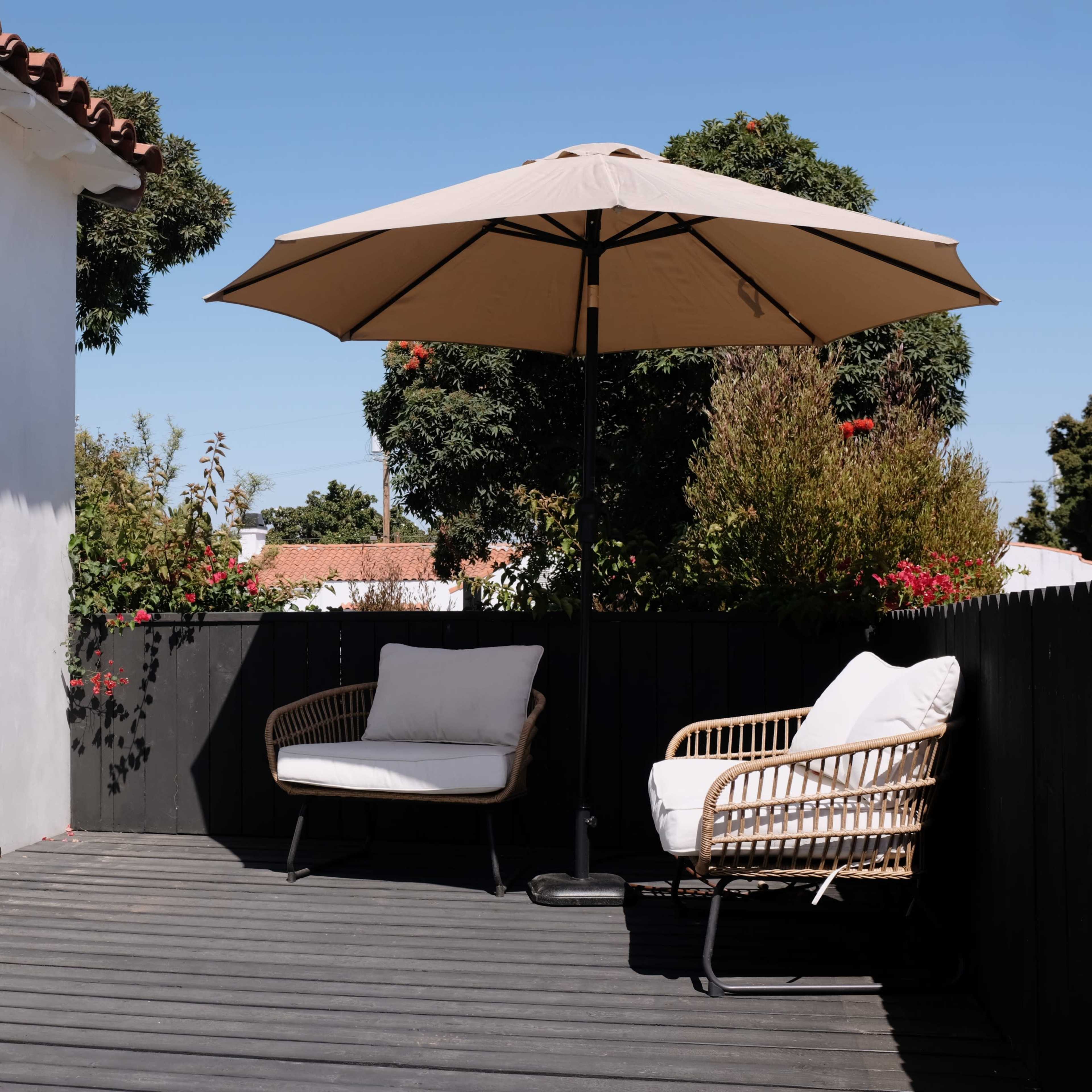 A patio area features two wicker chairs and a large umbrella beside a rustic white building.