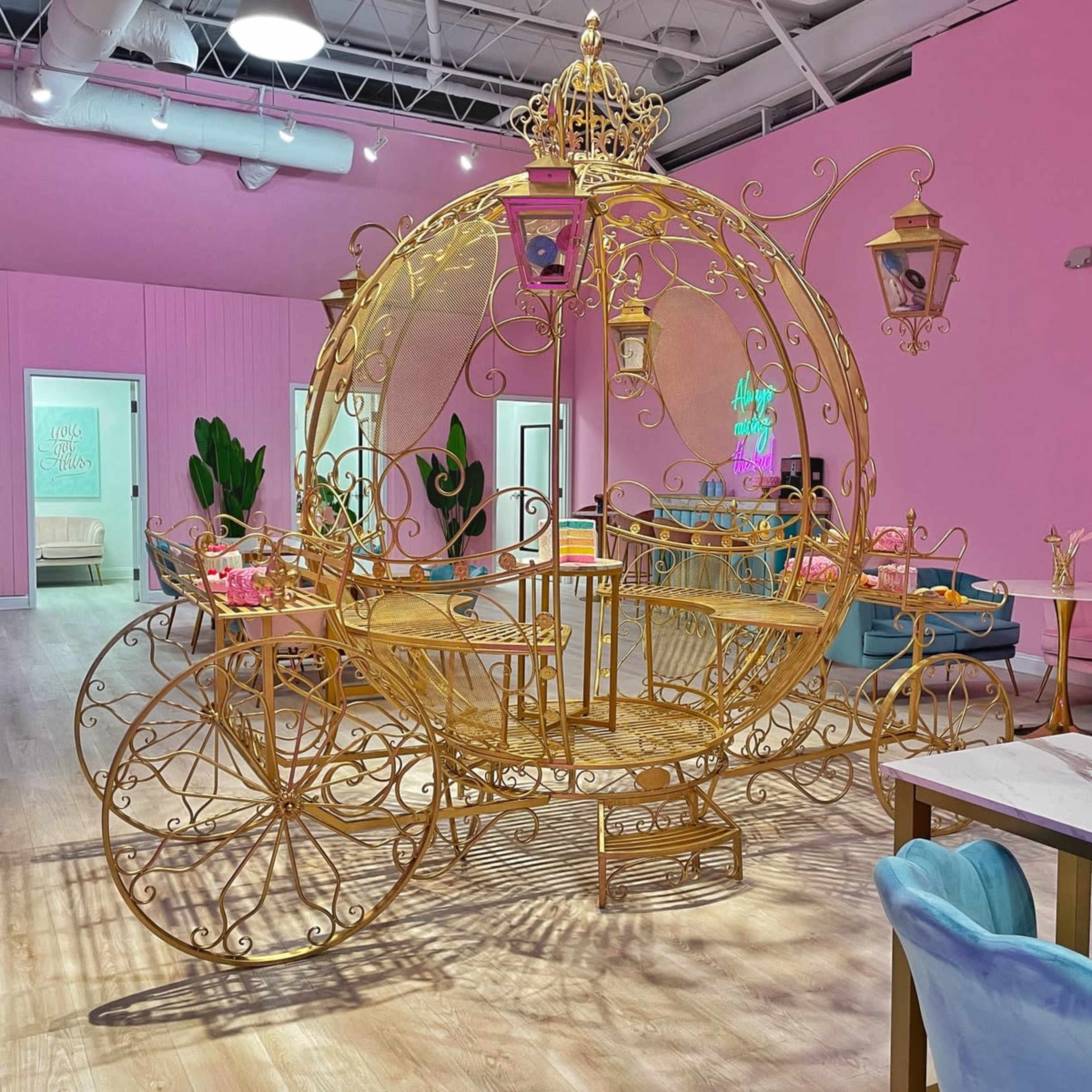 A gold carriage structure in a brightly colored room with pink walls and decorative elements.