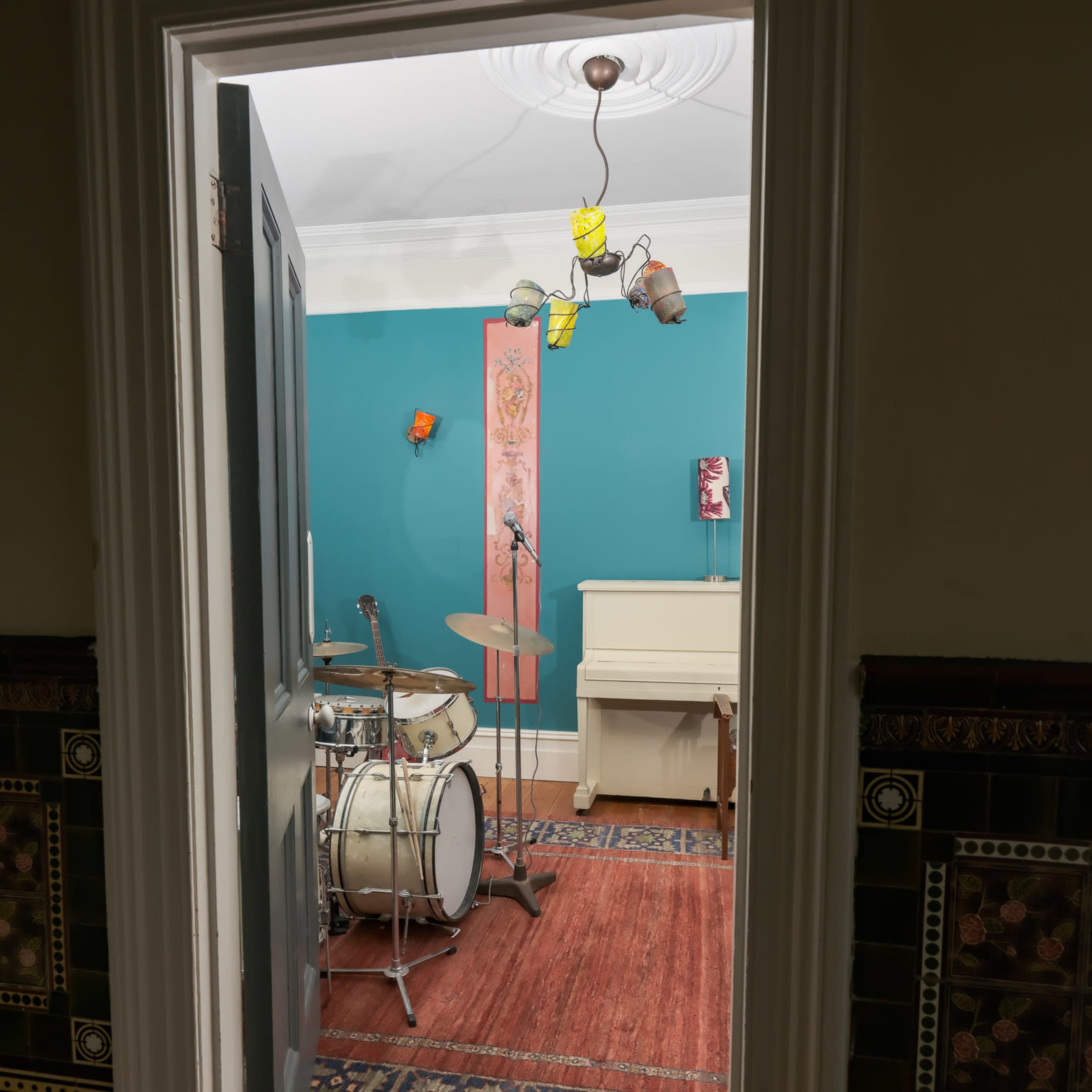 A doorway frames a colorful music room featuring a drum set, a small piano, and a decorated wall.