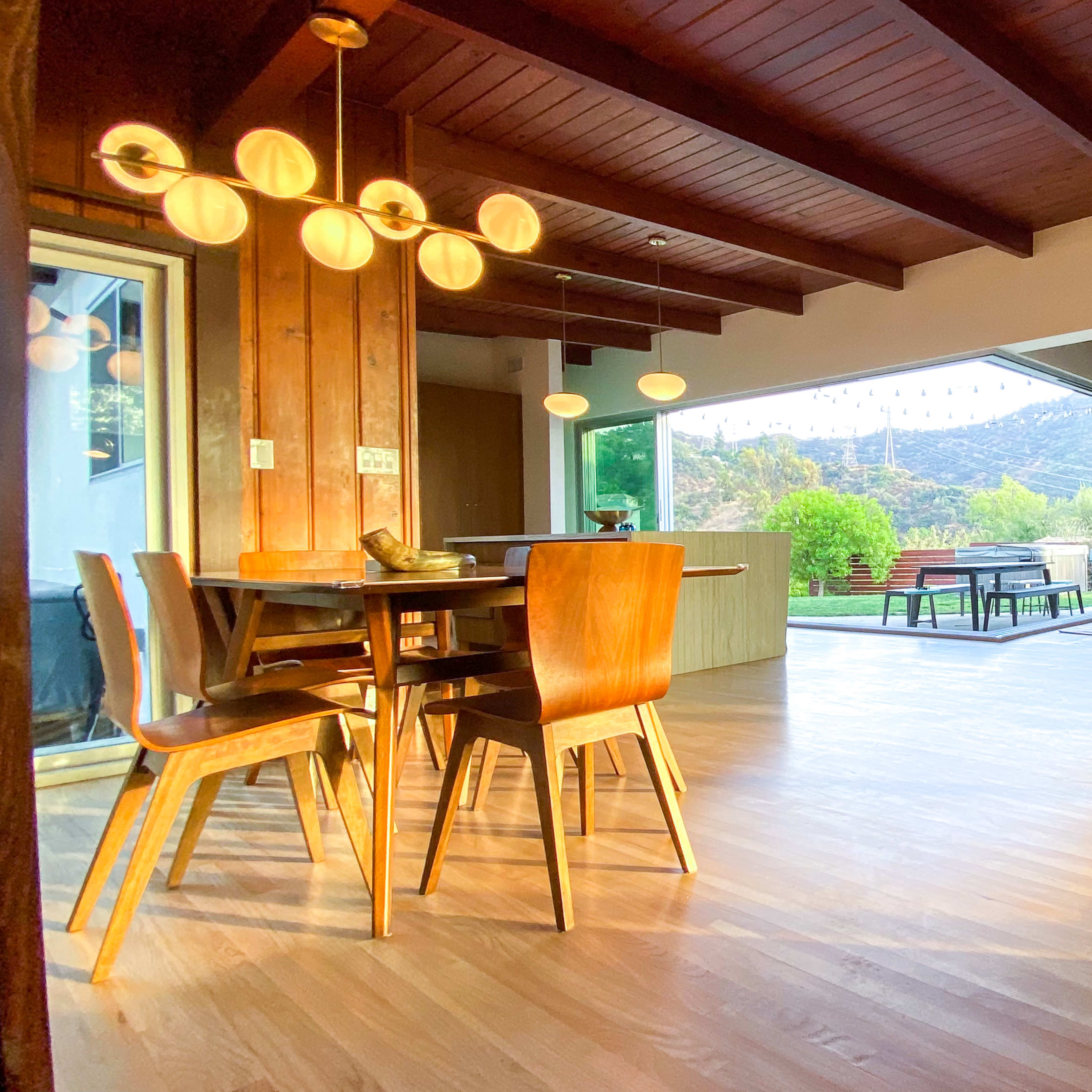 A dining area features wooden furniture and large windows that overlook a scenic outdoor space with mountains in the background.