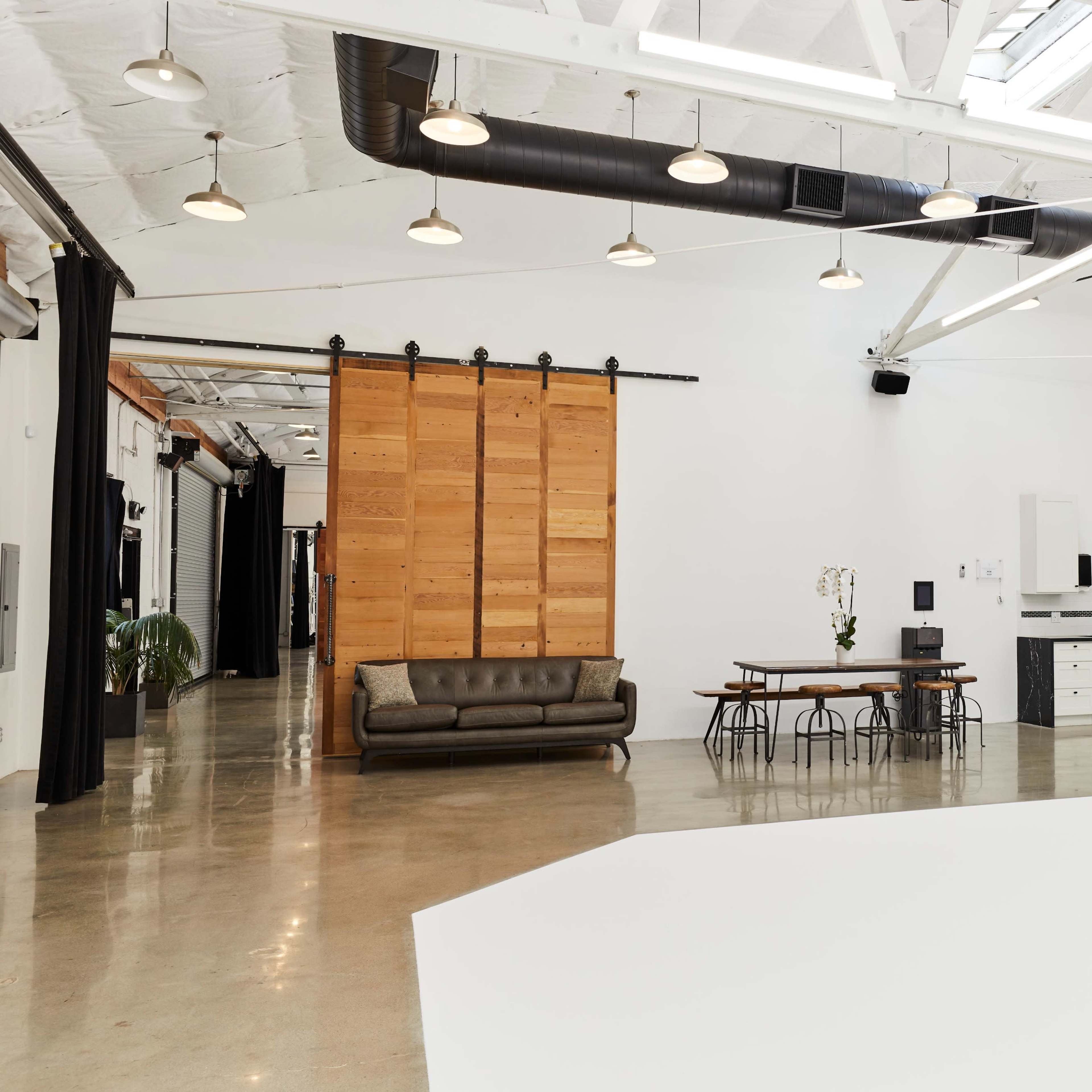 A spacious, brightly lit interior features a kitchen with a dining table, a sofa, and wooden sliding doors.