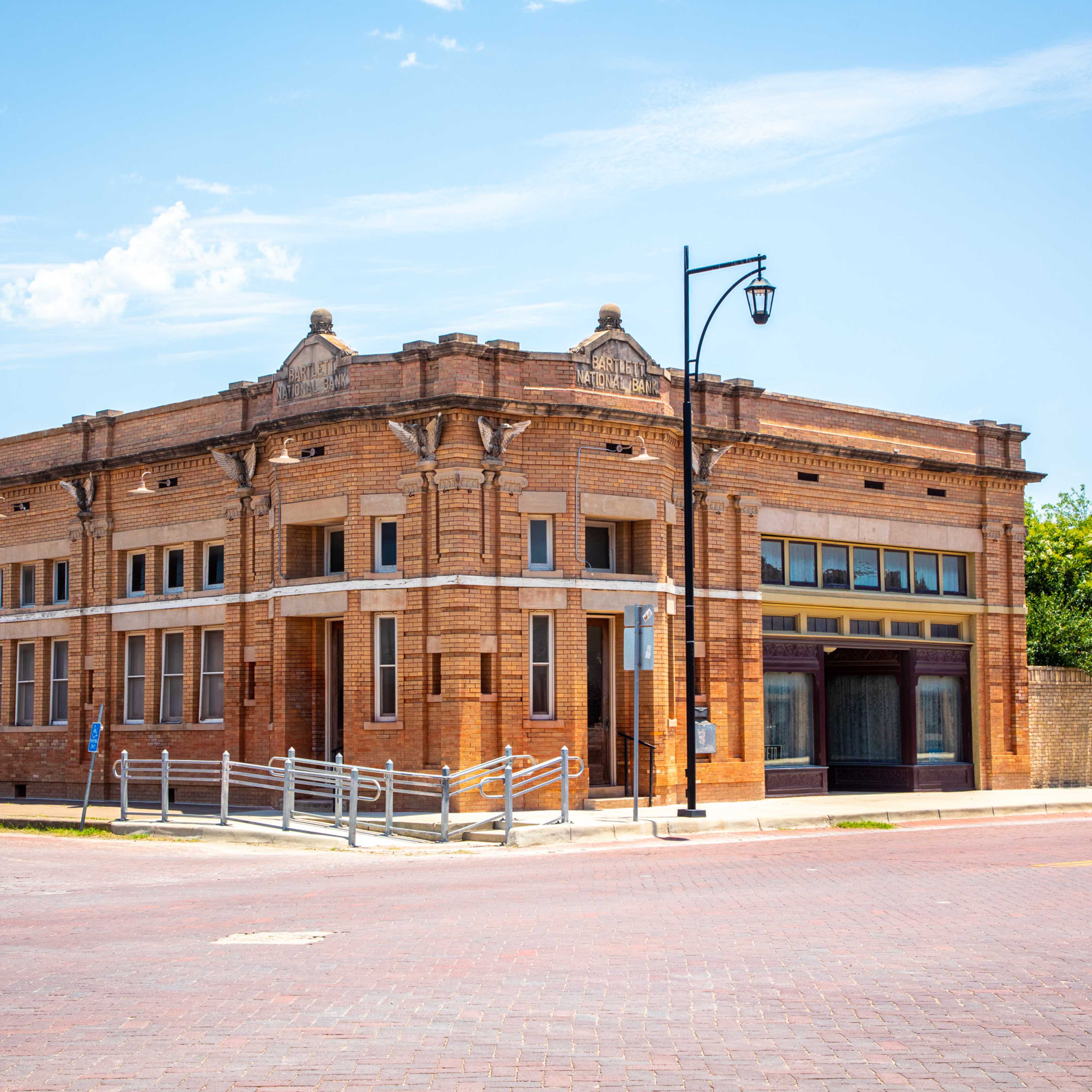 A historic brick building with decorative architectural features, situated at the corner of a street with a clear blue sky above.