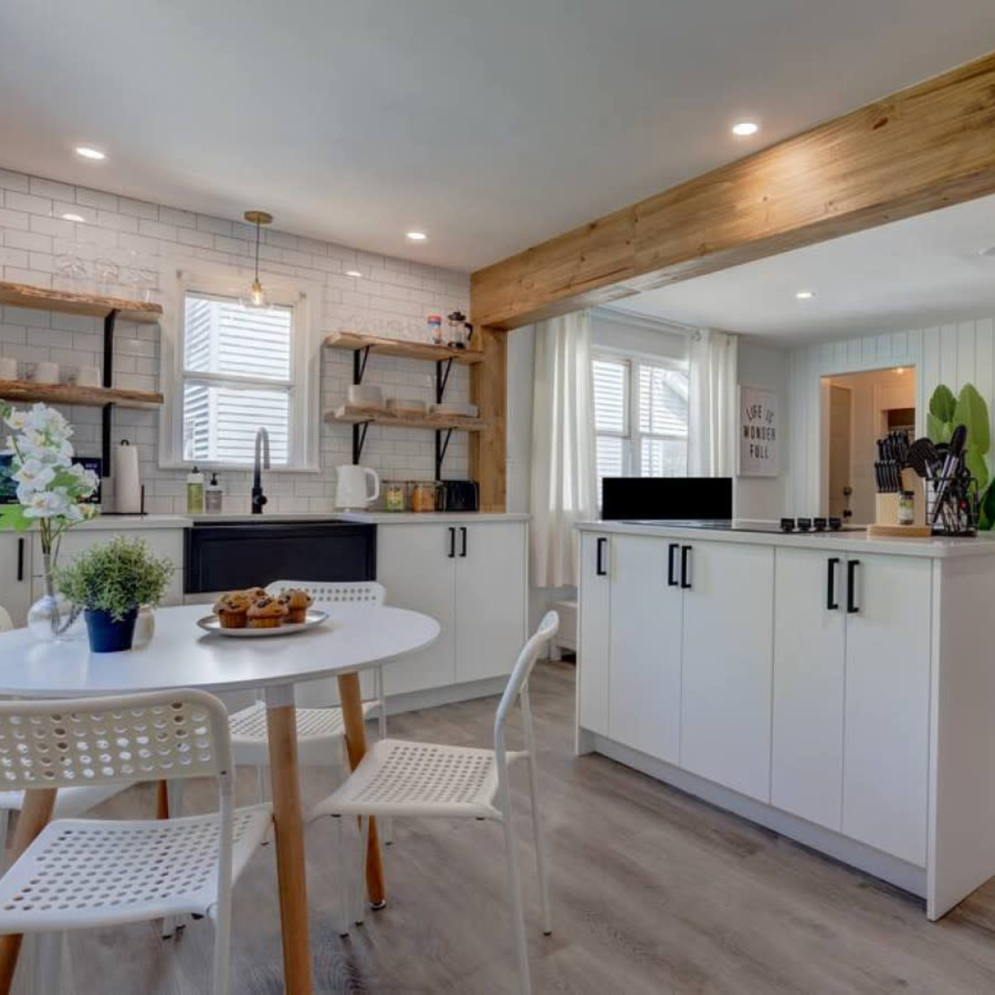 The kitchen features white cabinetry, open wooden shelves, and a round table with four chairs.