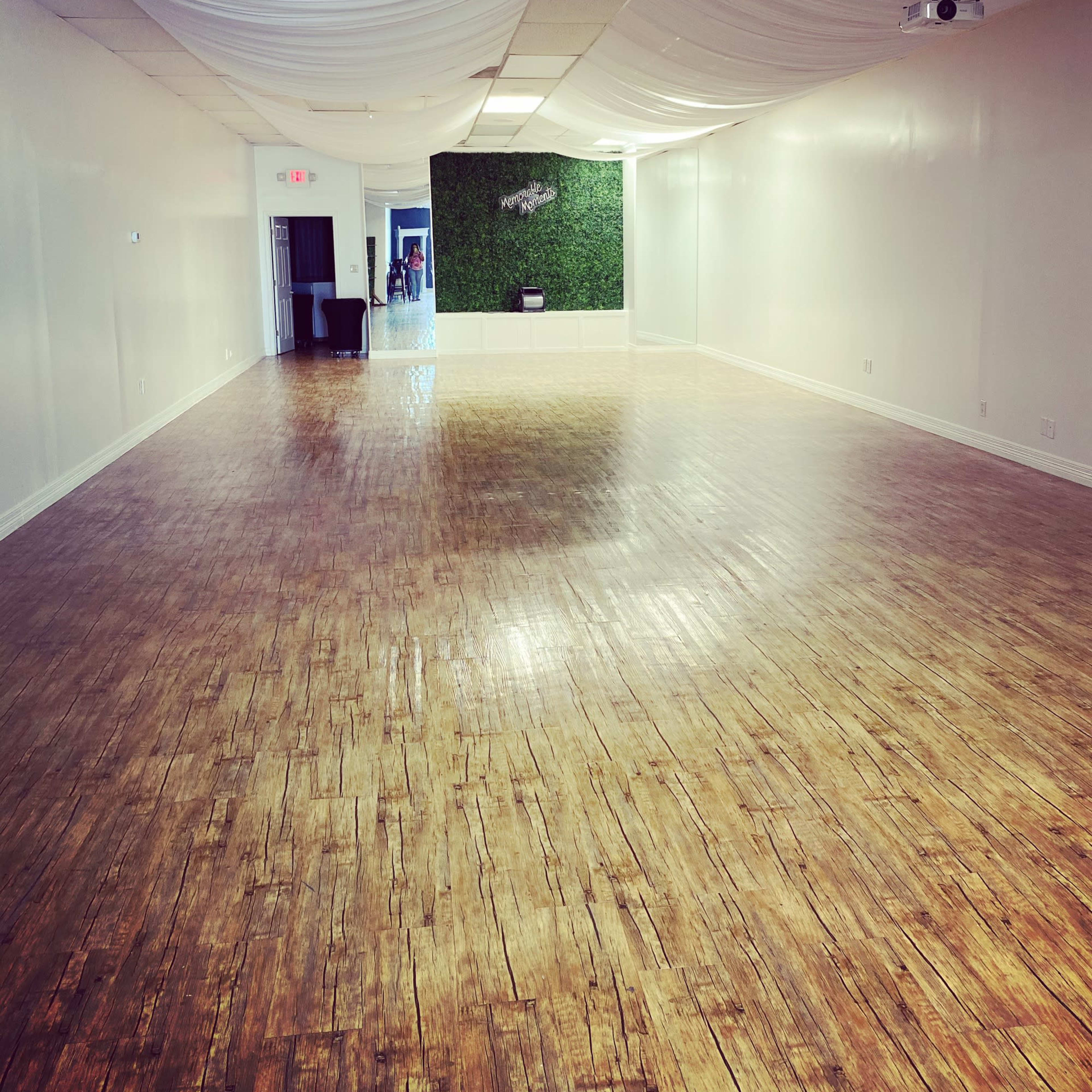 A spacious room with wooden flooring, white walls, and decorative drapery on the ceiling.