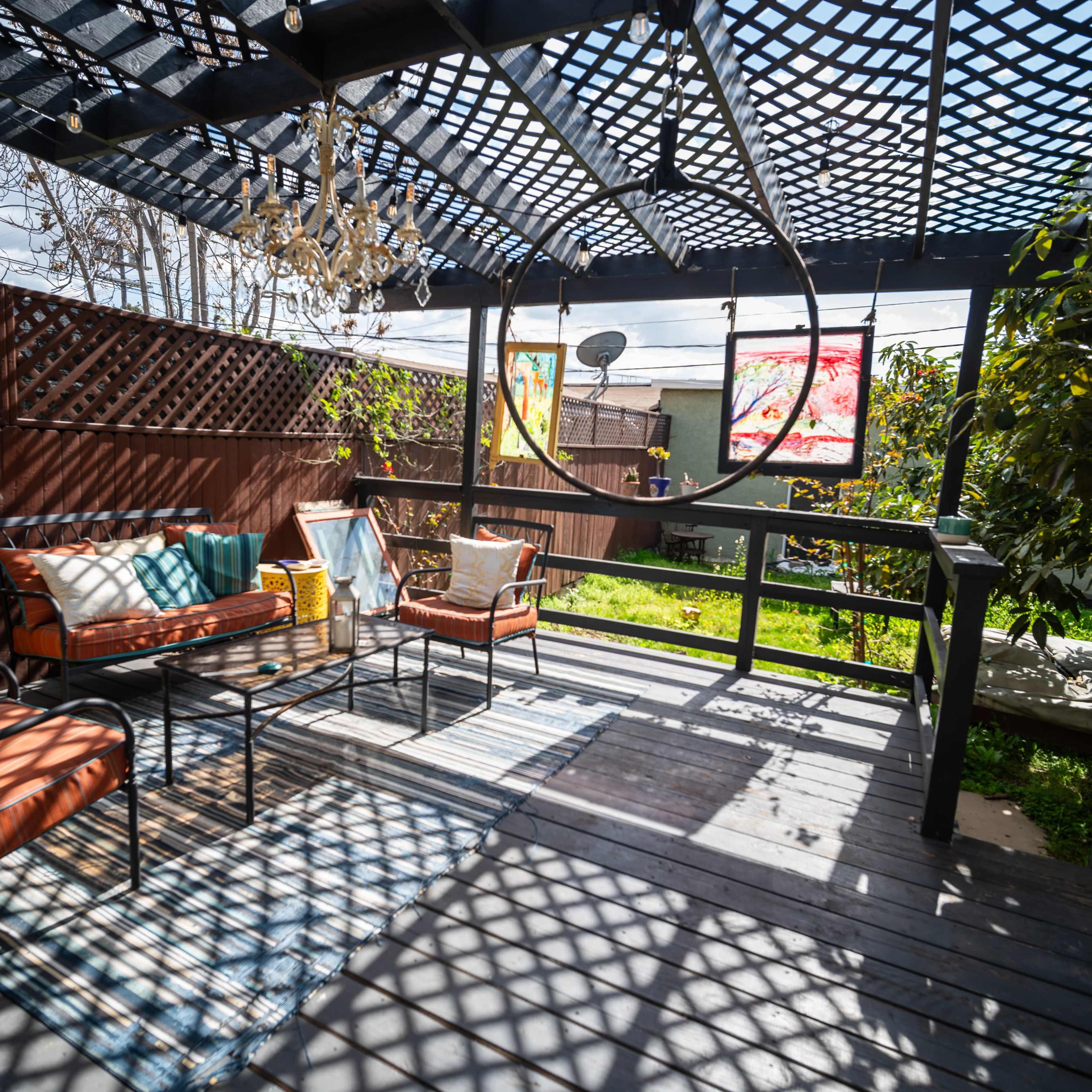 A patio with seating arrangements under a lattice roof, featuring a swing and several decorative cushions.
