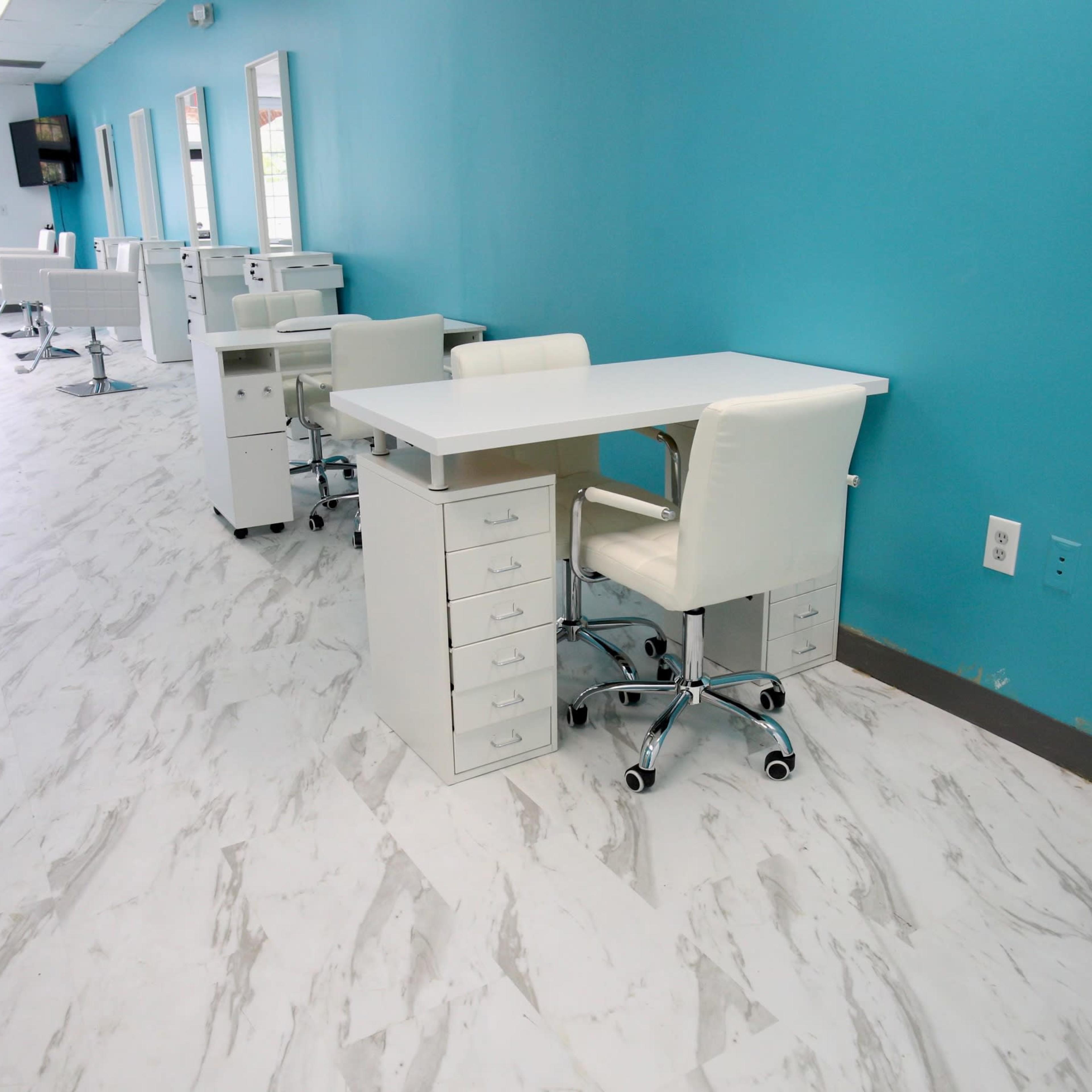 A brightly lit salon interior with white workstations and chairs against a turquoise wall.