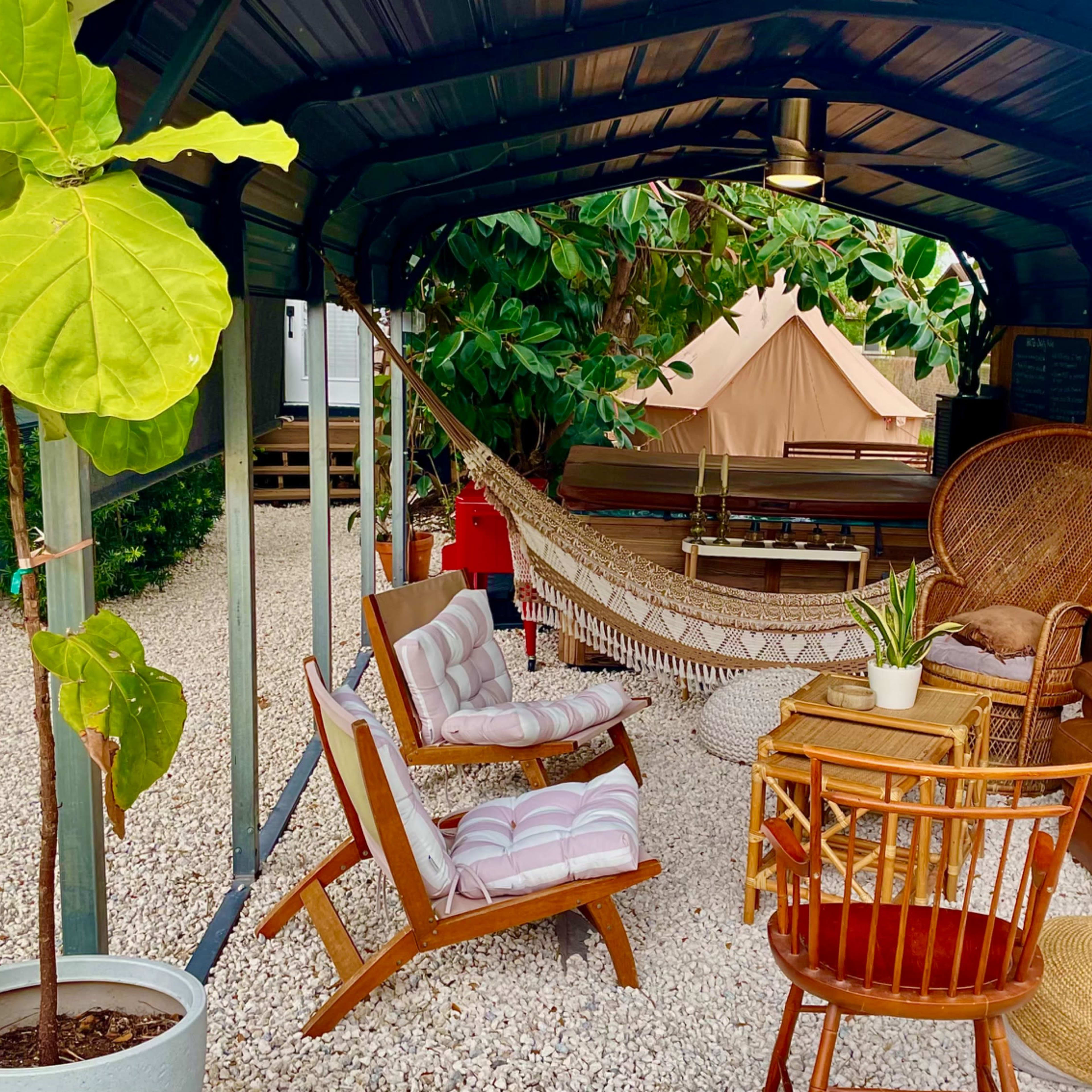 A cozy outdoor seating area with a hammock, various chairs, and potted plants under a metal canopy.