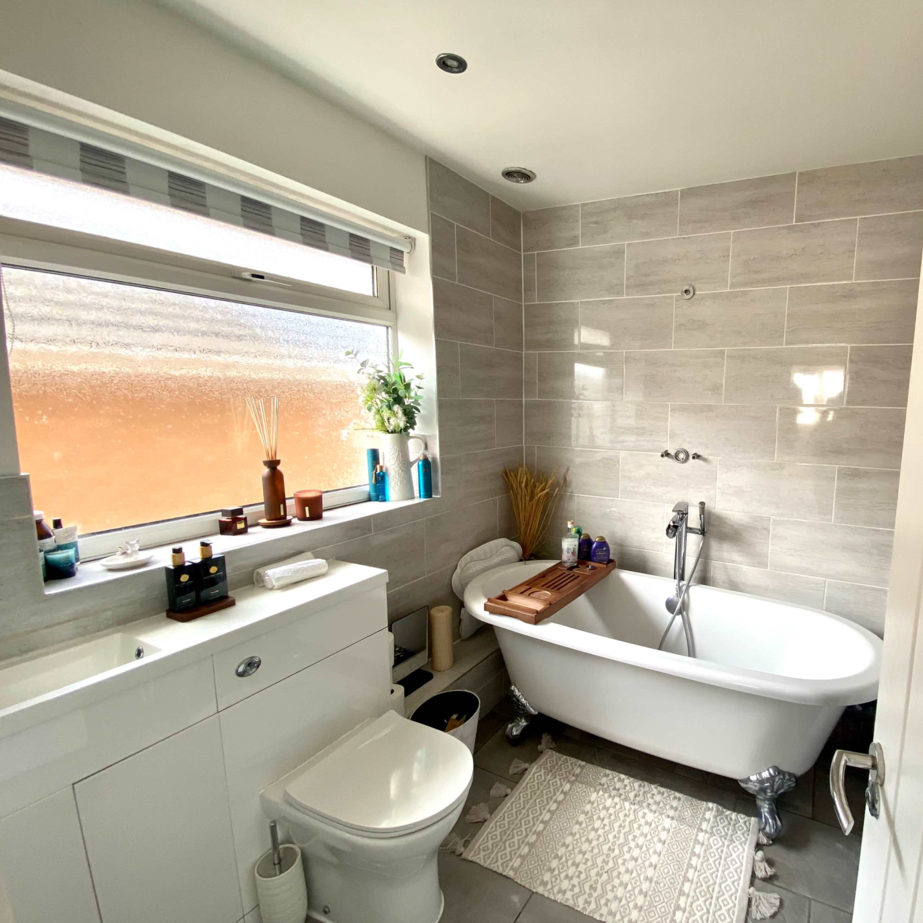 A modern bathroom featuring a freestanding white bathtub, a sink with storage cabinets, and a large window with natural light.