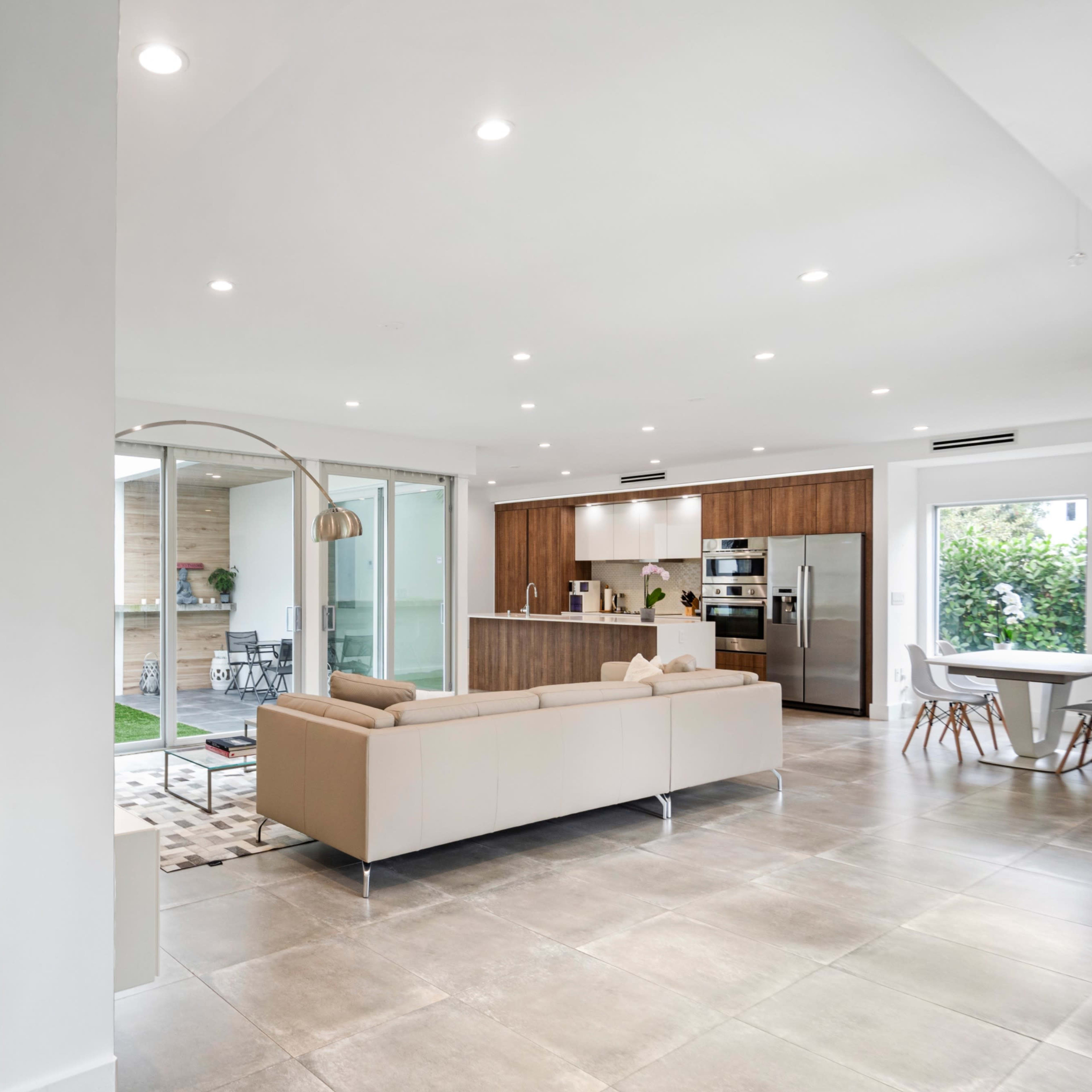 A modern open-concept living space features a staircase, a beige sofa, and a kitchen with wooden cabinets and stainless steel appliances.