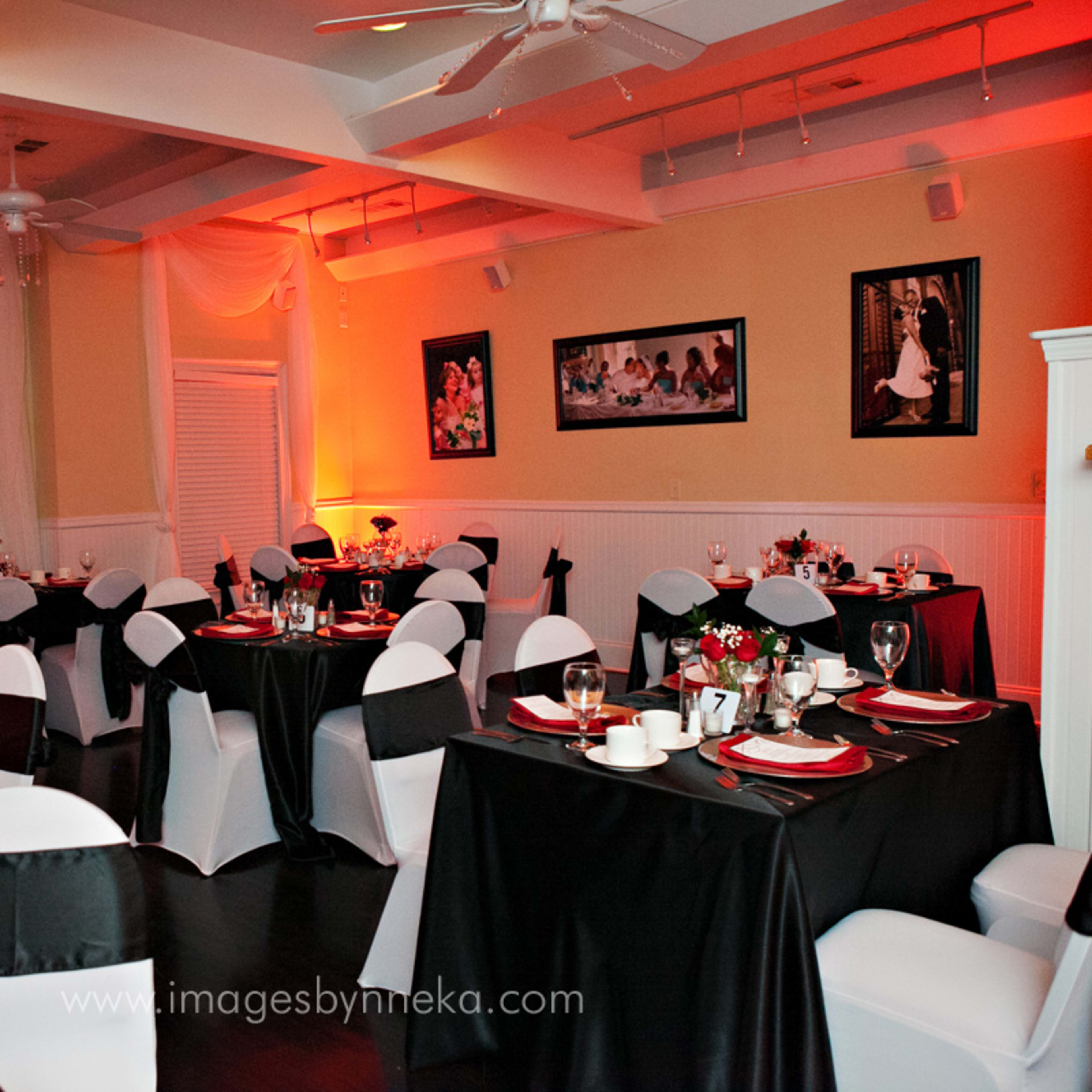 A dining room is set with black and white tablecloths, neatly arranged tableware, and decorative floral centerpieces under warm lighting.