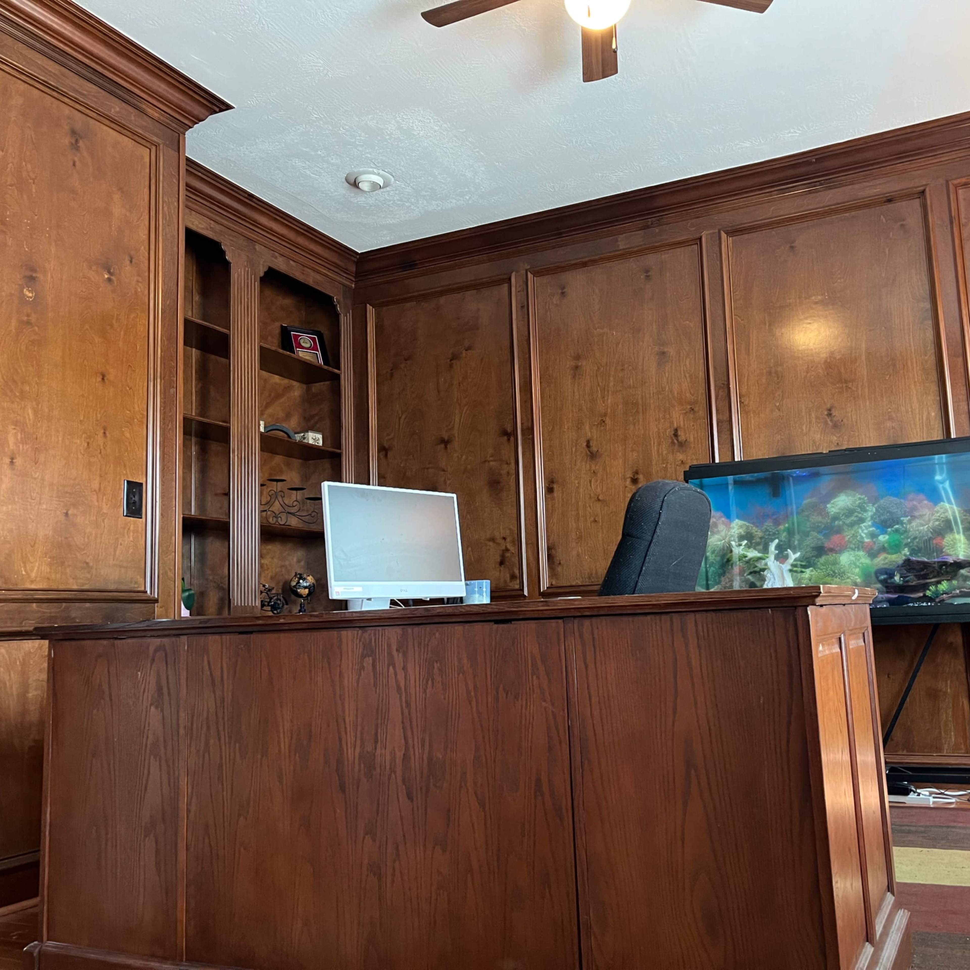 A wooden office with a large desk, a computer monitor, and an aquarium in one corner.