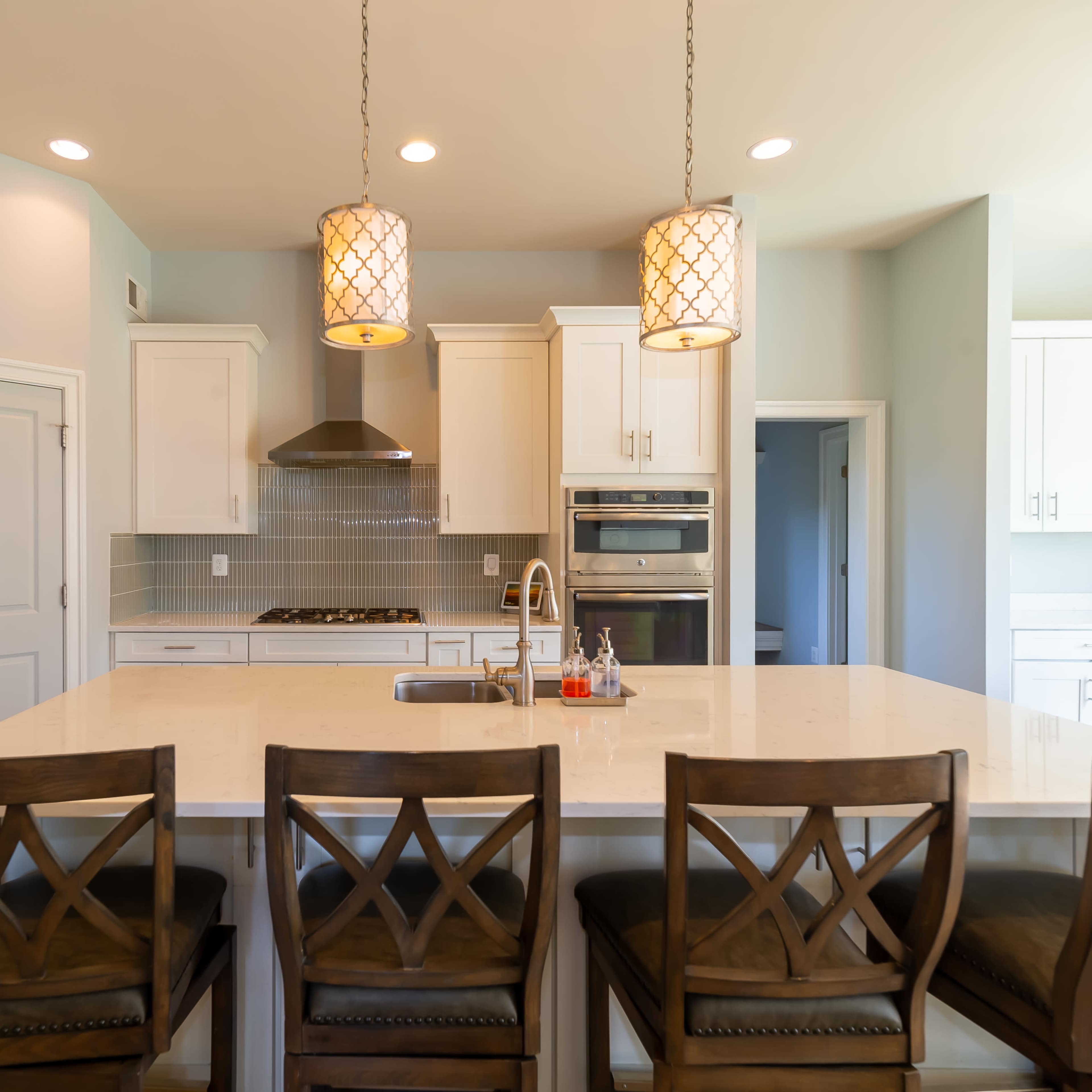 A modern kitchen features a central island with barstools, stainless steel appliances, and pendant lighting above.