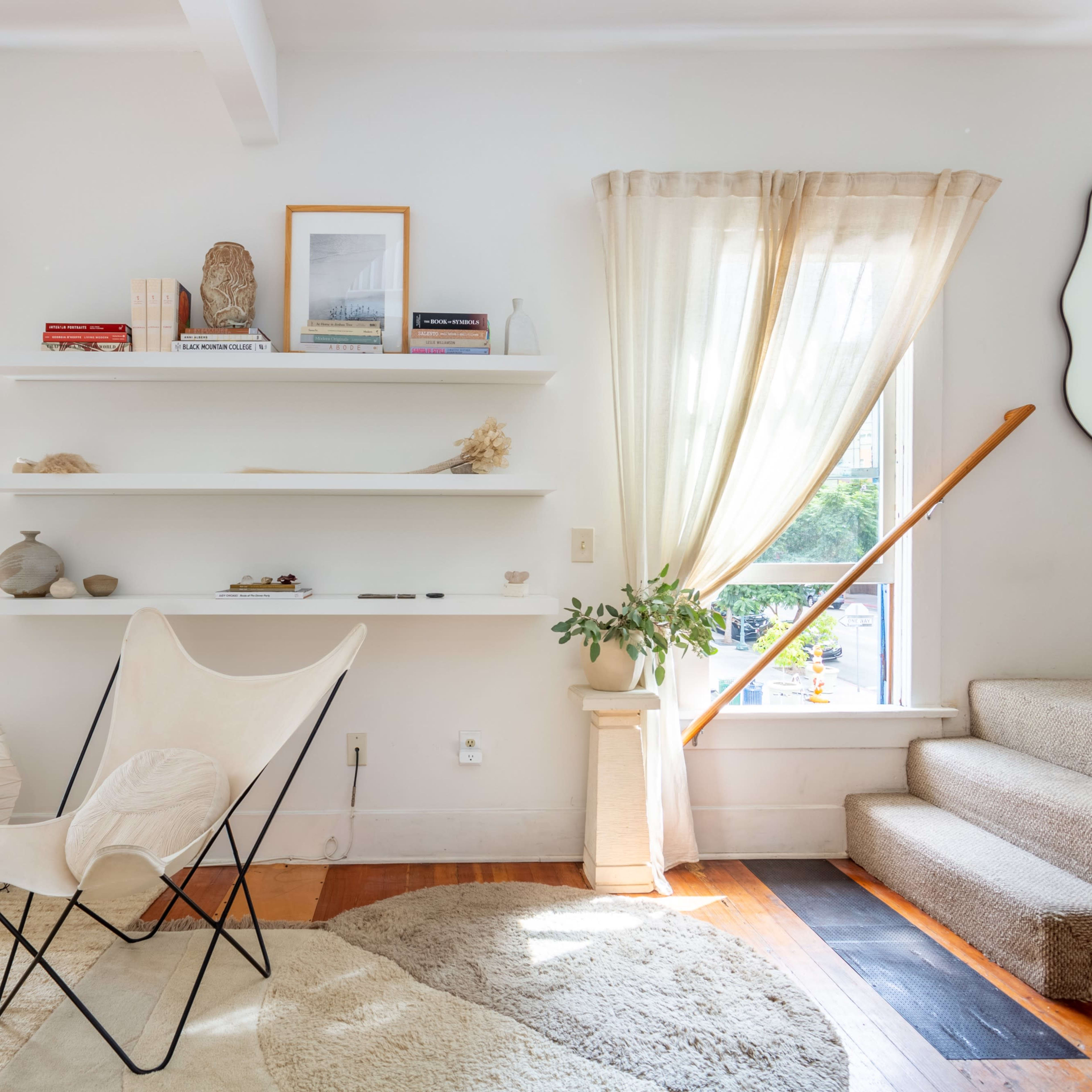 A bright living room featuring a butterfly chair, shelves with decorative items, and steps leading to an upper level.