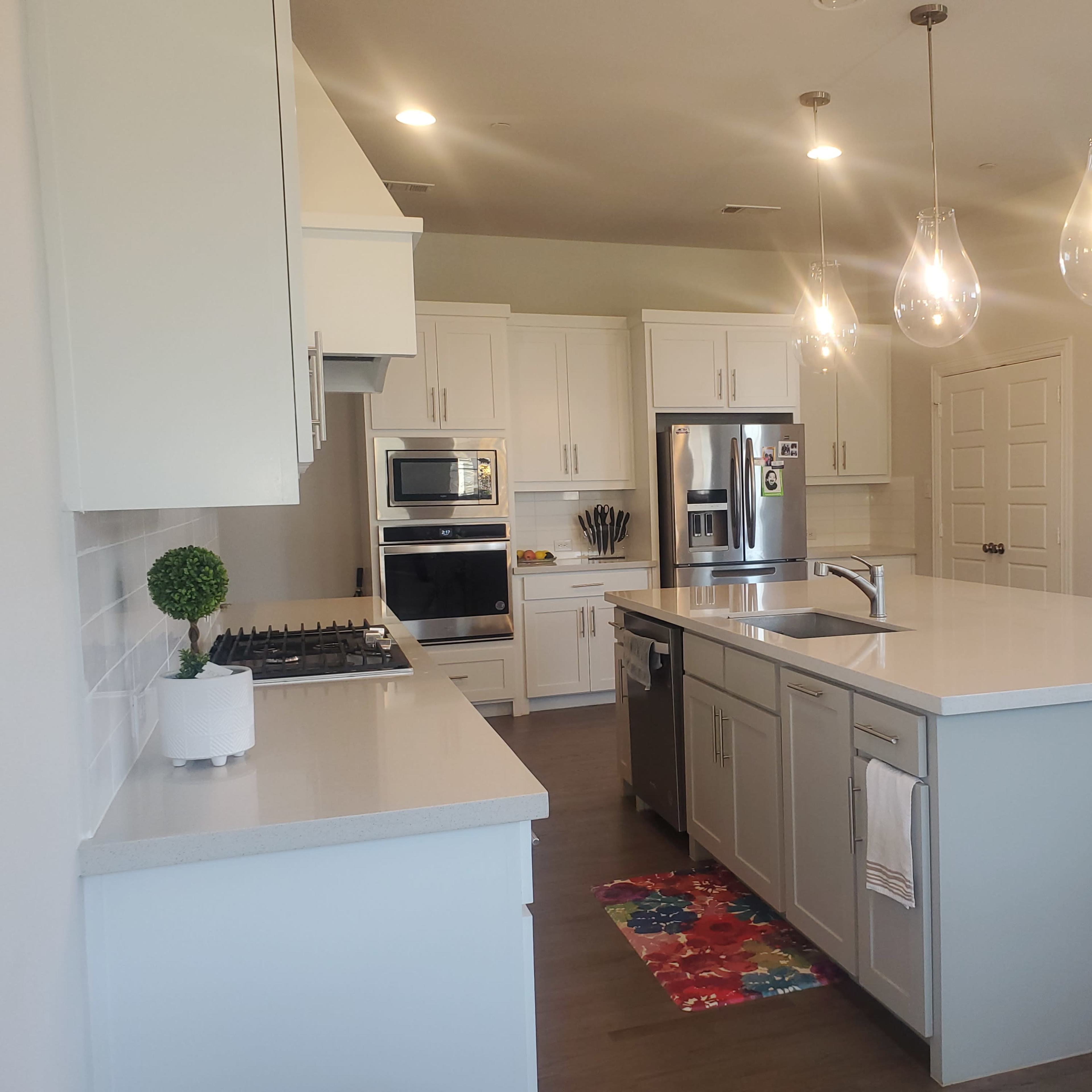 The kitchen features white cabinetry, stainless steel appliances, a central island with a sink, and modern pendant lighting.