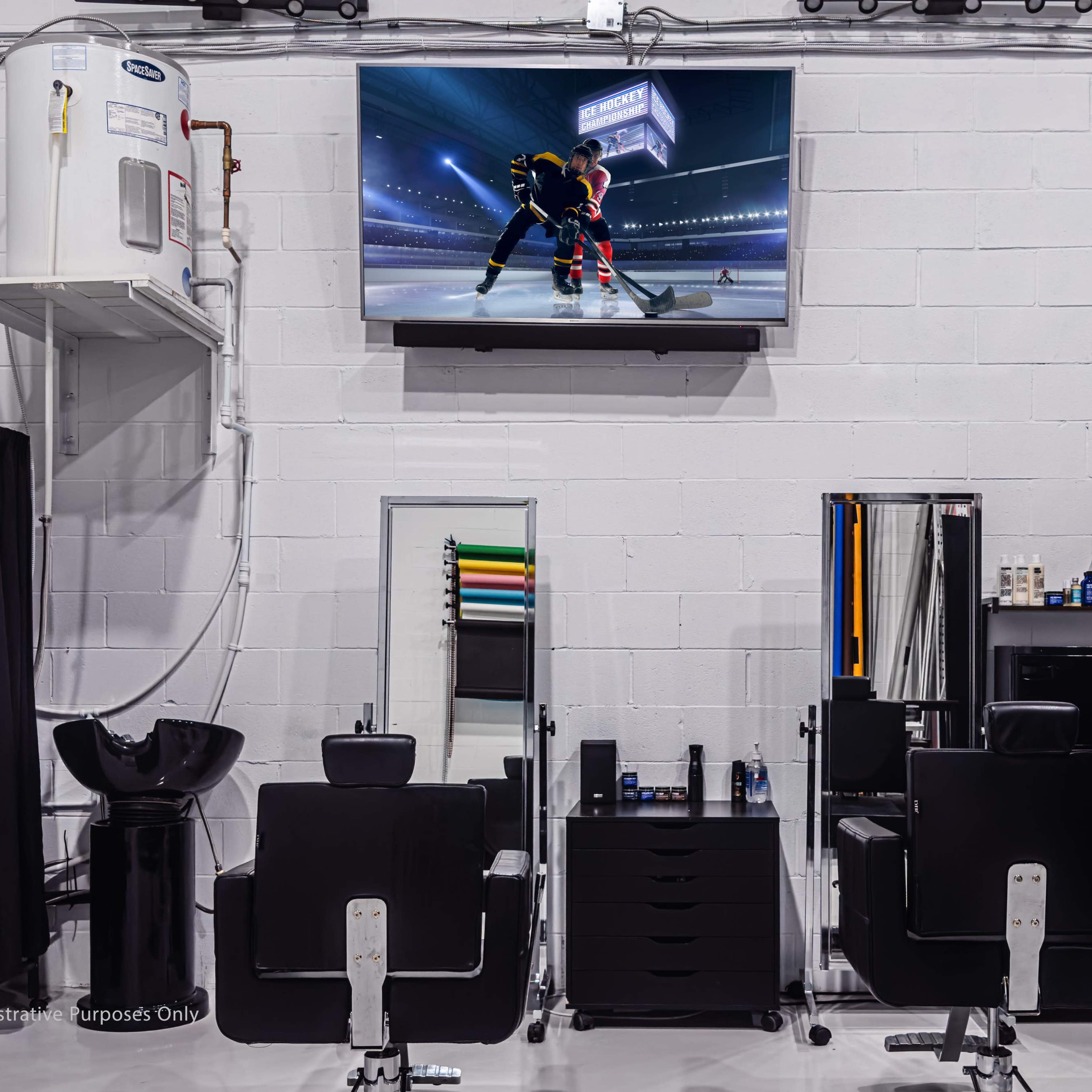 A modern hair salon with several styling stations, a large television displaying a hockey game, and a wall-mounted sink.