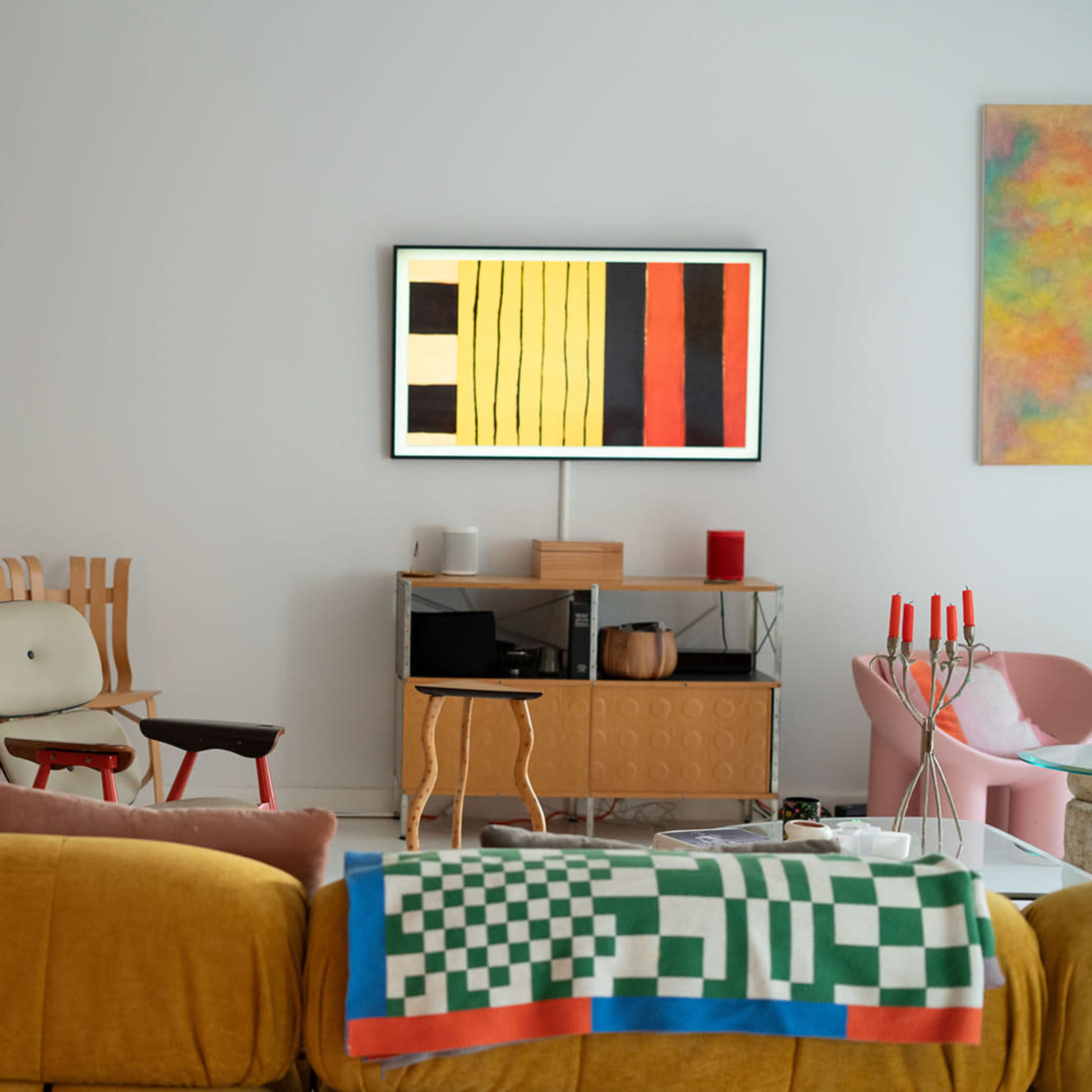 A modern living room features colorful artwork, contemporary furniture, and a television mounted on a white wall.