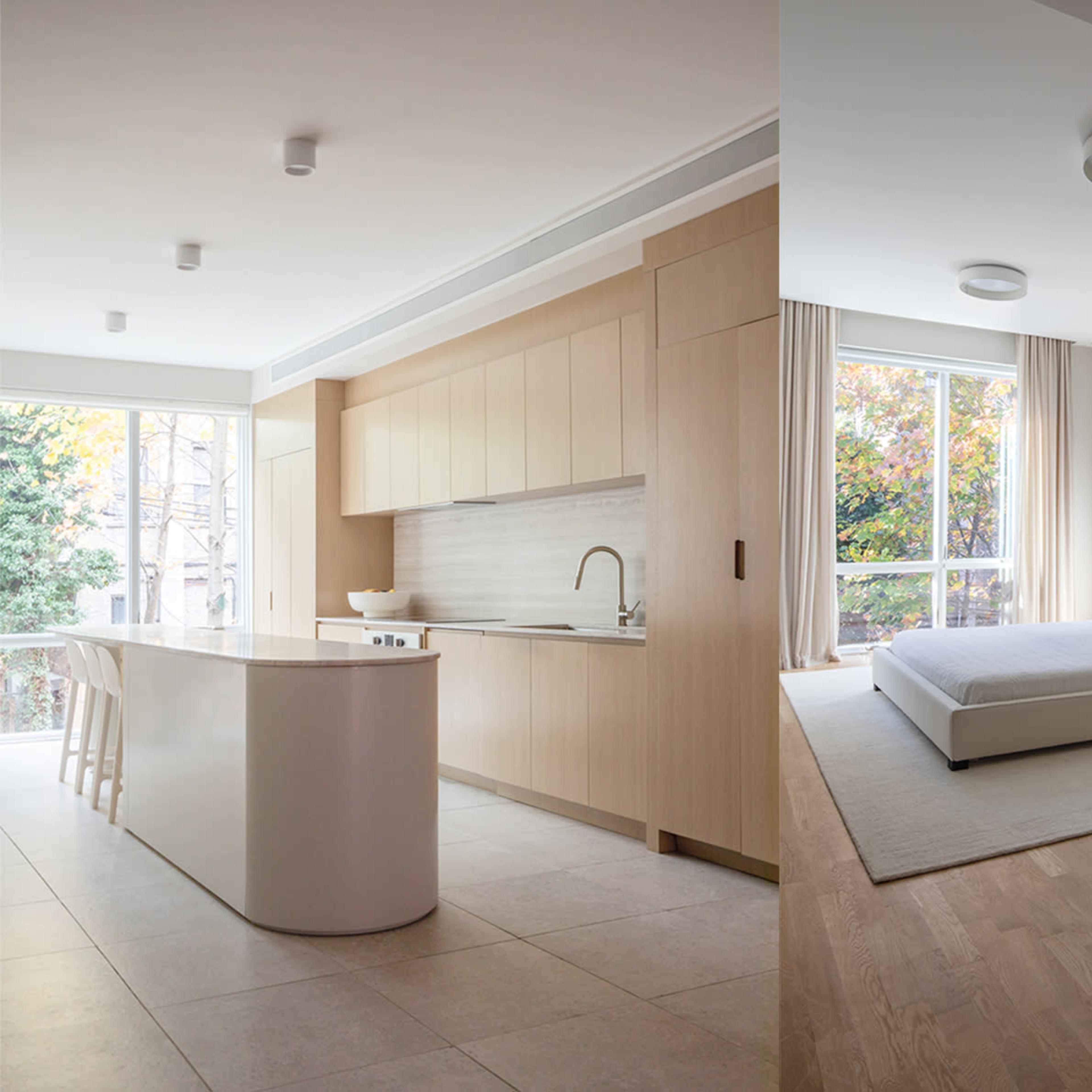 A modern kitchen with light wood cabinets and a white island on one side, and a minimalist bedroom with a bed and large window on the other.