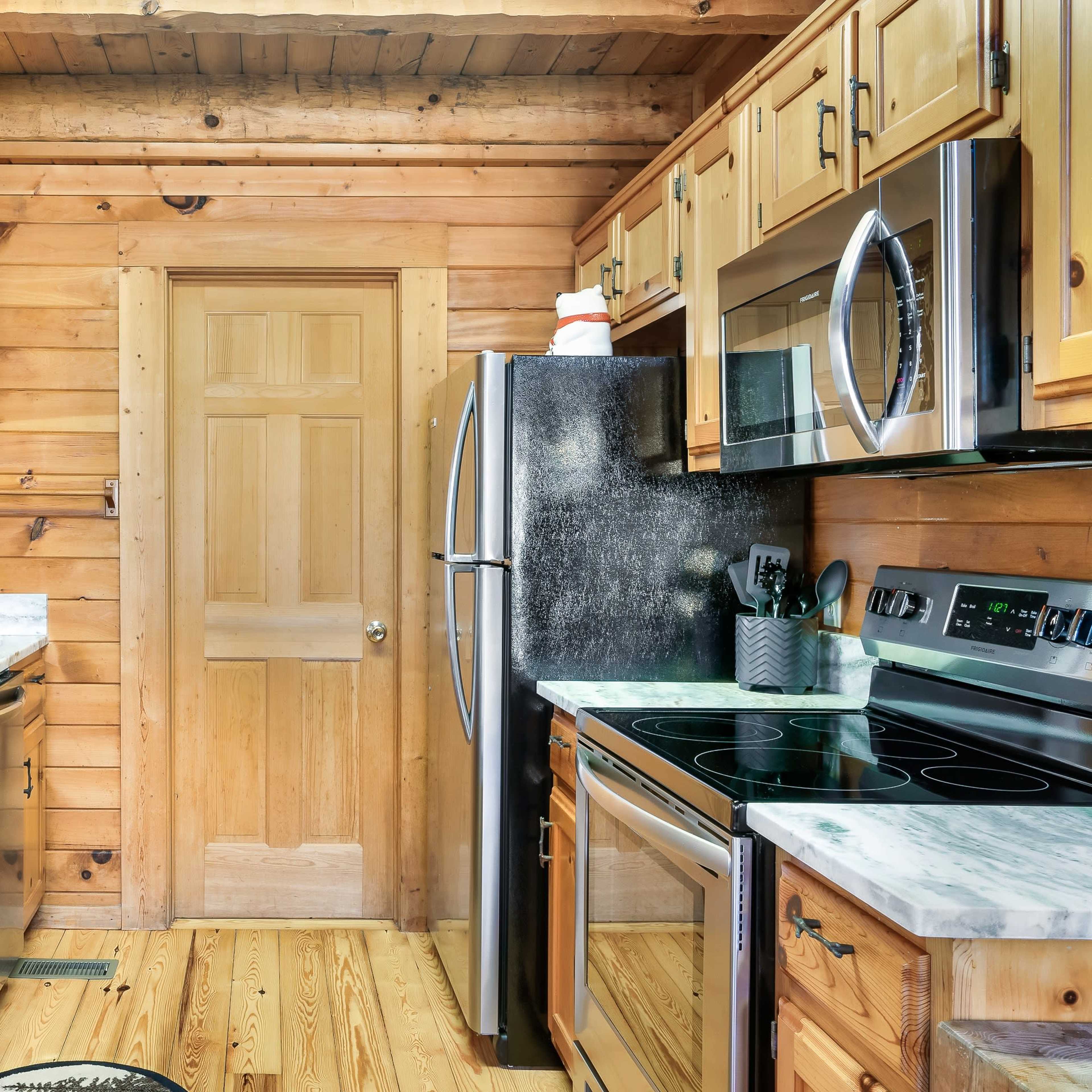 A wooden kitchen featuring a stainless steel refrigerator, an oven, and a sink with a marble countertop.