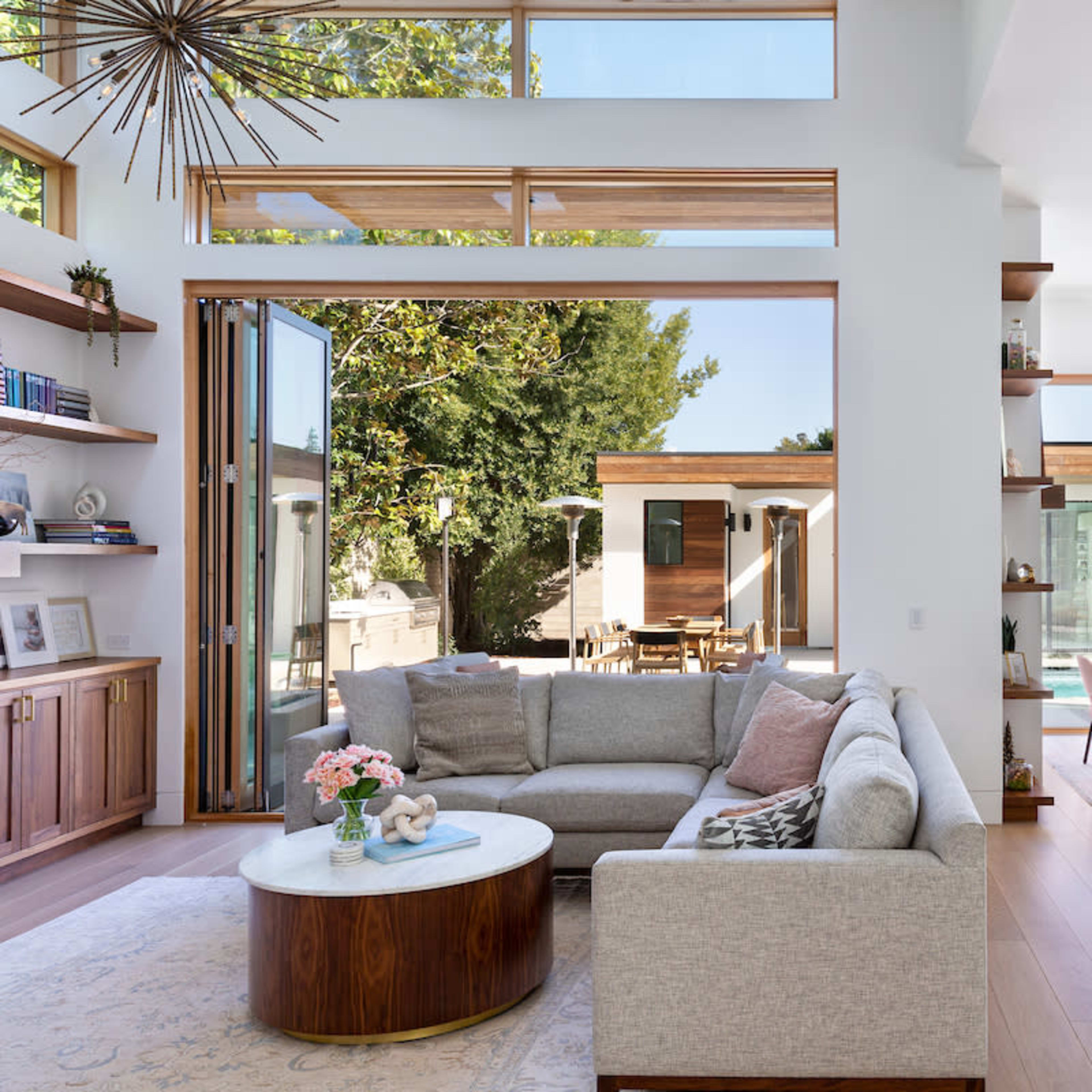 A modern open-concept living space with a light gray sectional sofa, a round coffee table, and large glass doors leading to an outdoor area.