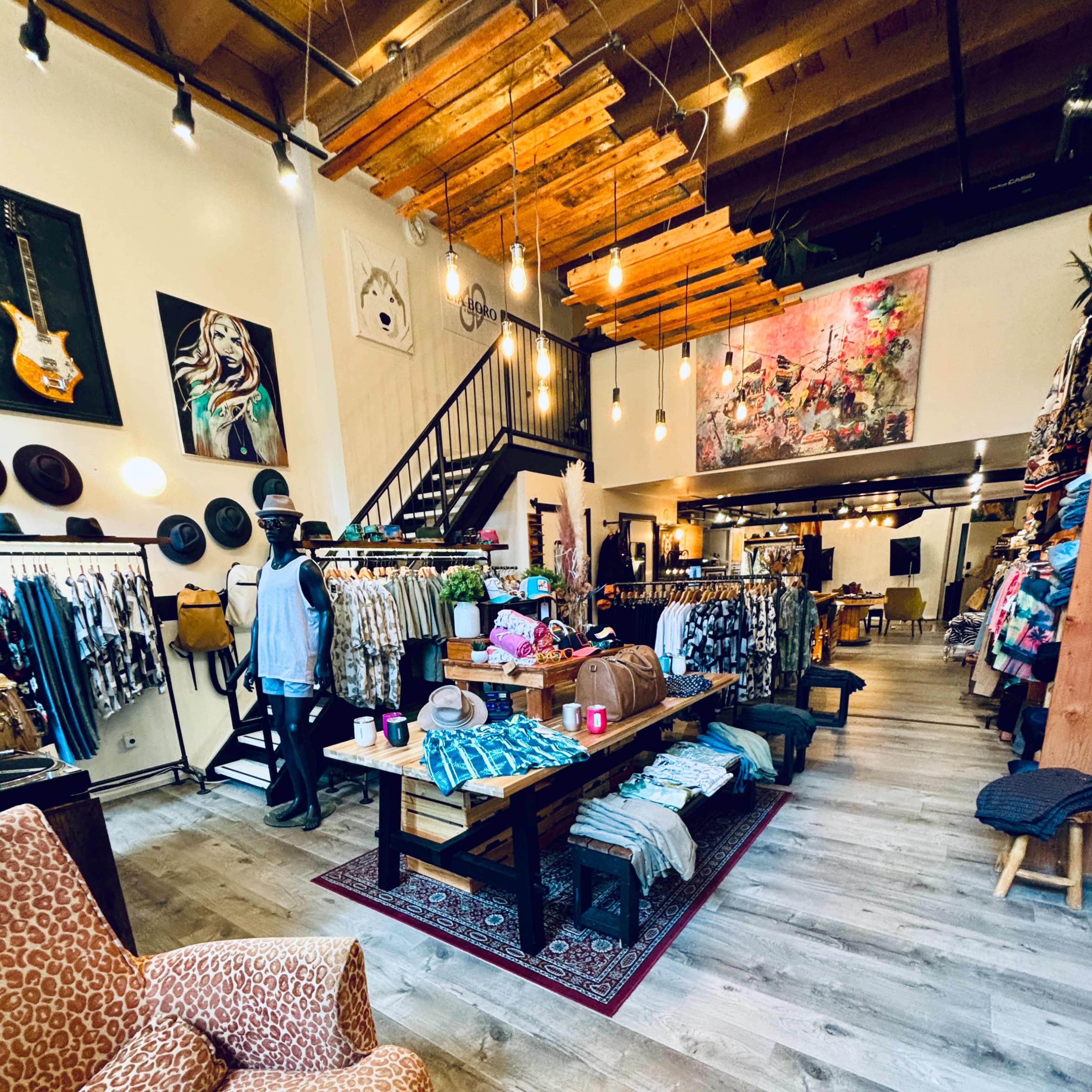 A clothing boutique interior featuring racks of apparel, a patterned rug, and a cozy seating area with a patterned chair.