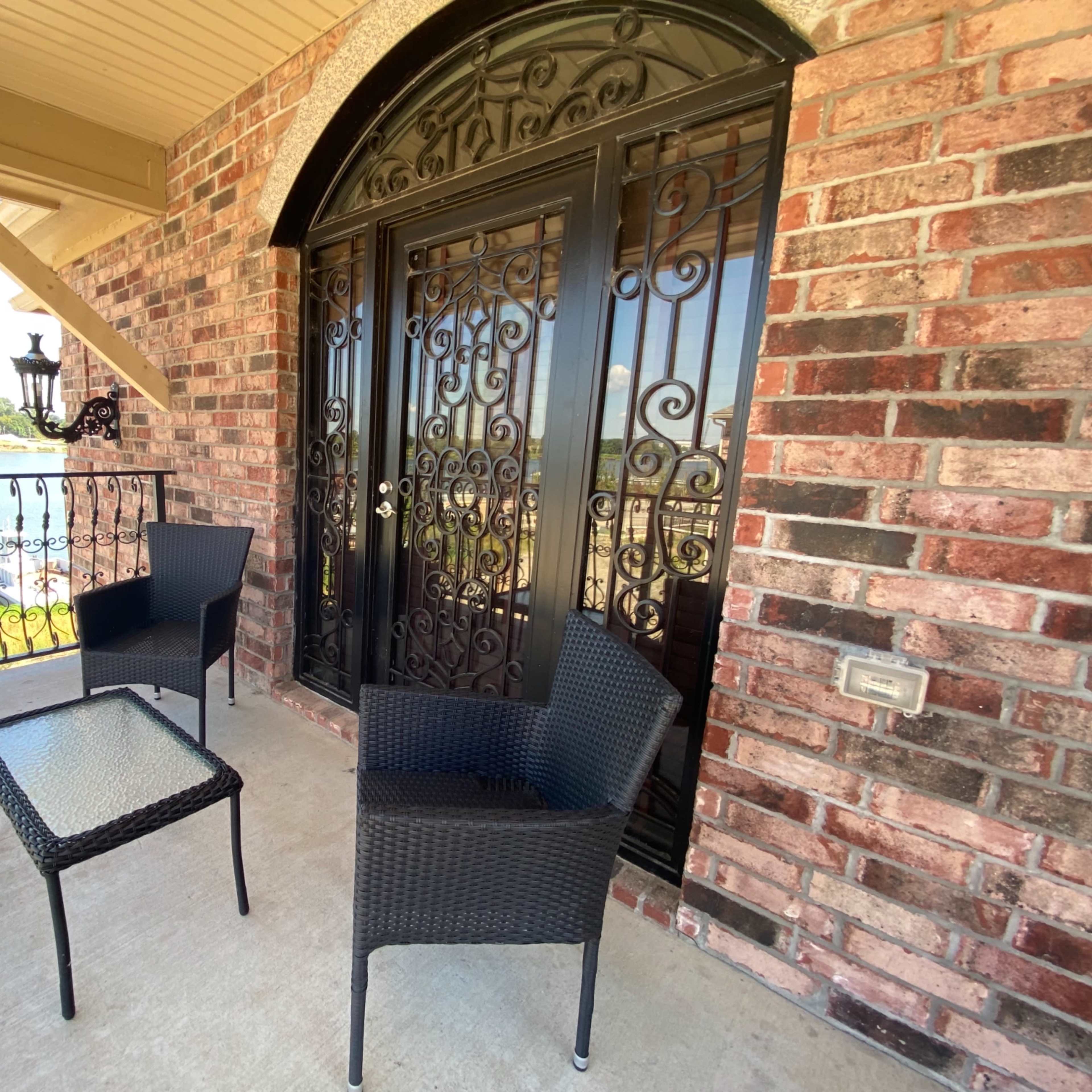 A balcony with two wicker chairs and a glass-topped table, overlooking a body of water.