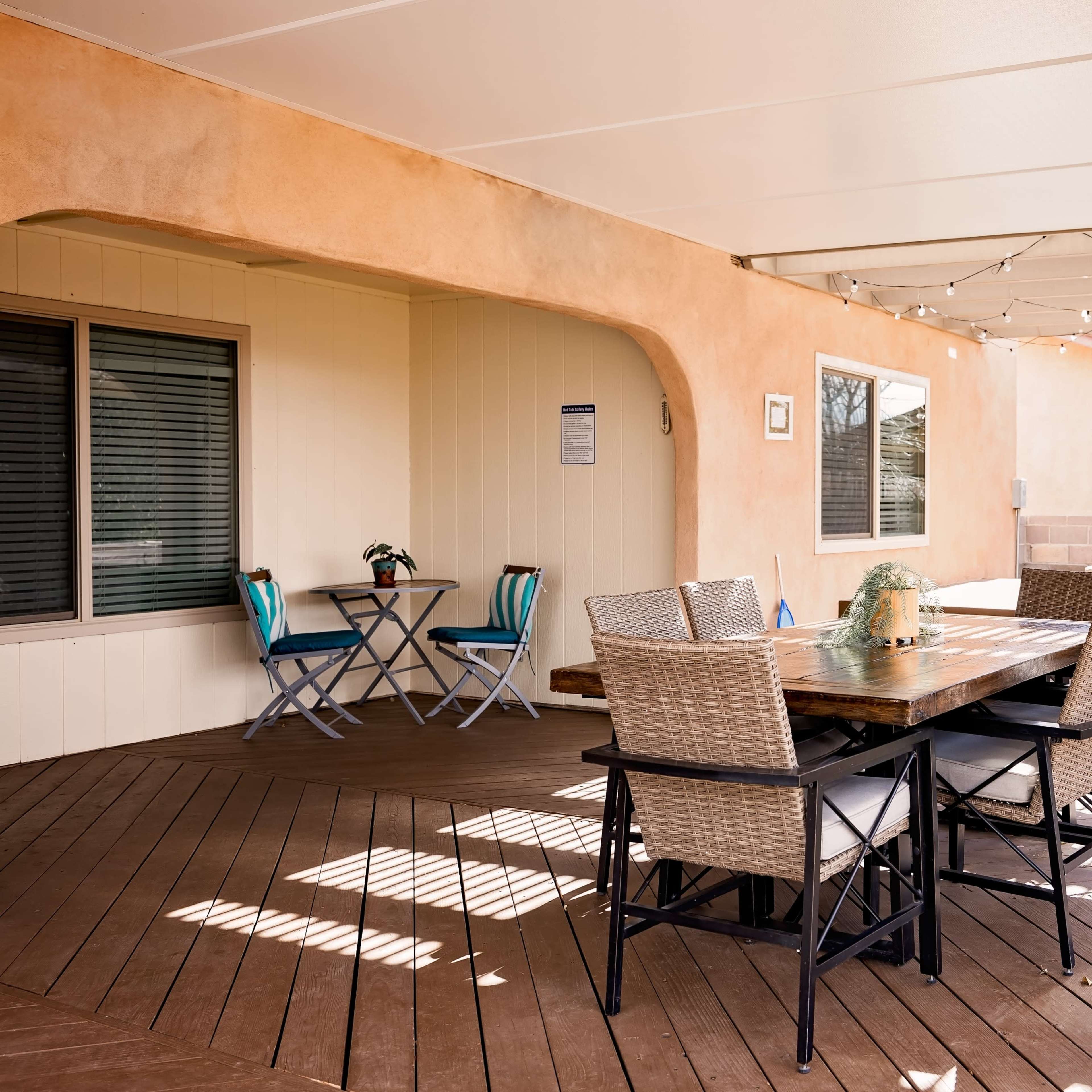 A covered patio with a wooden dining table and chairs, alongside a small seating area and a hot tub.