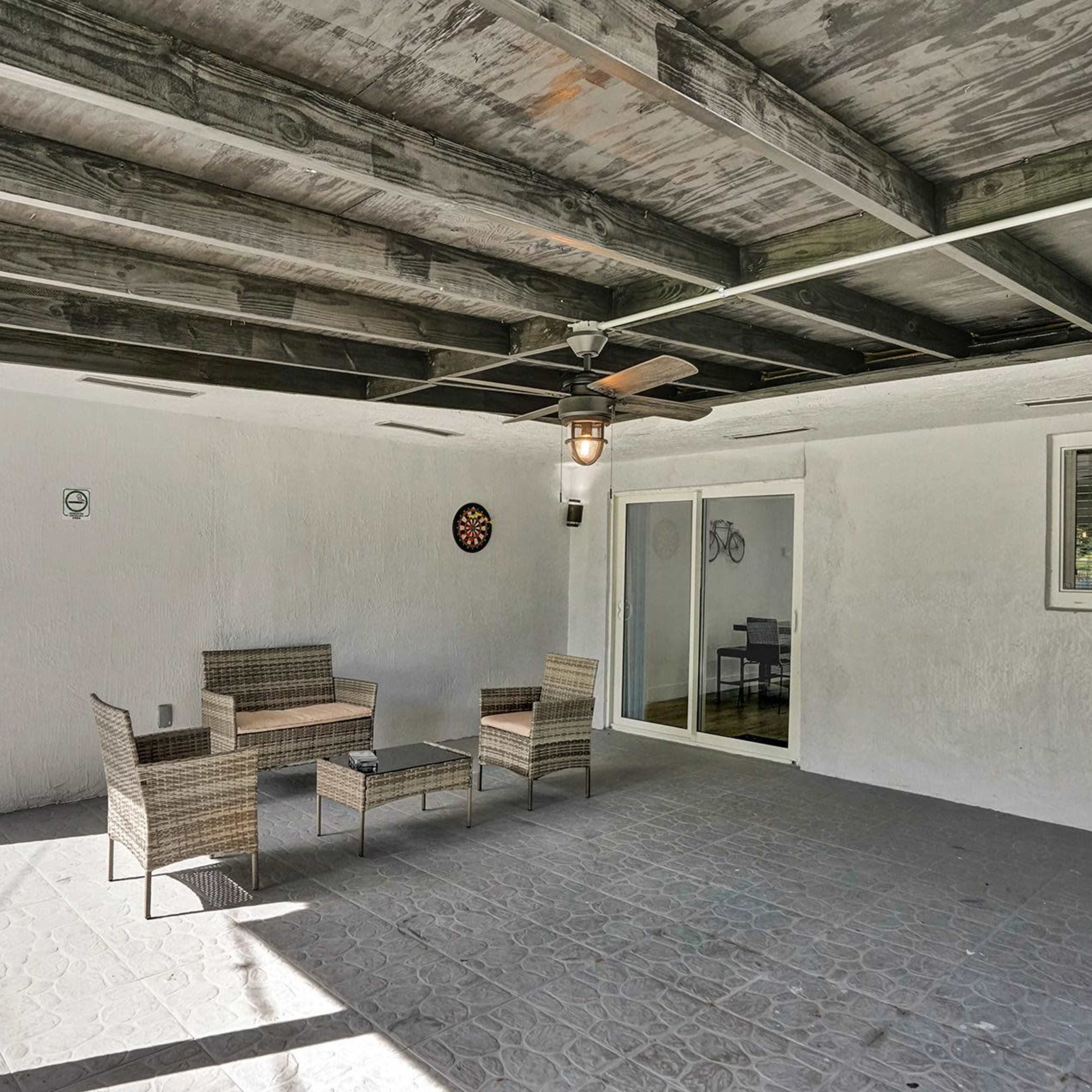A covered outdoor space with a ceiling fan, a small table, and four wicker chairs, adjacent to a glass sliding door.