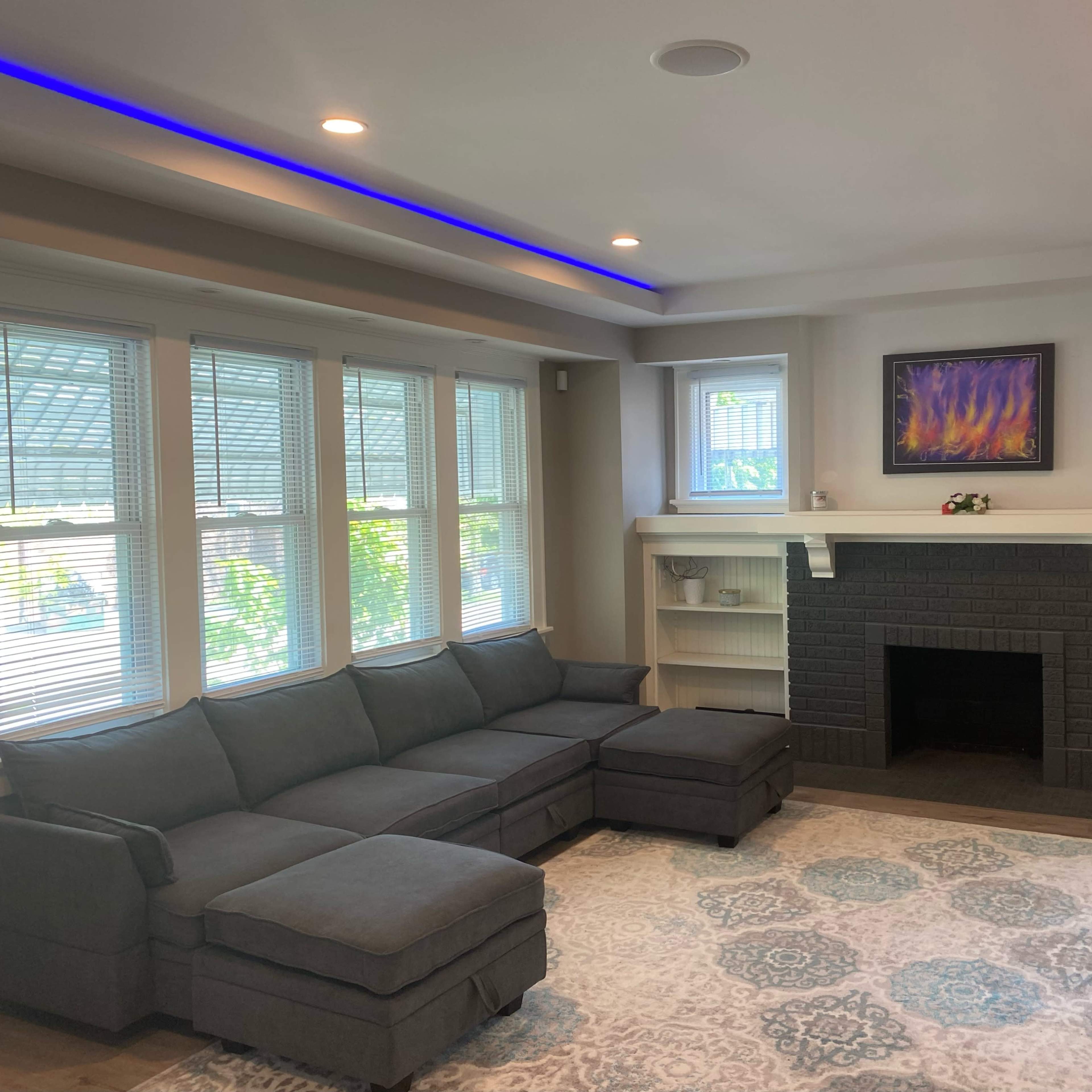 A modern living room with a gray sectional sofa, a black brick fireplace, and large windows that allow natural light to fill the space.