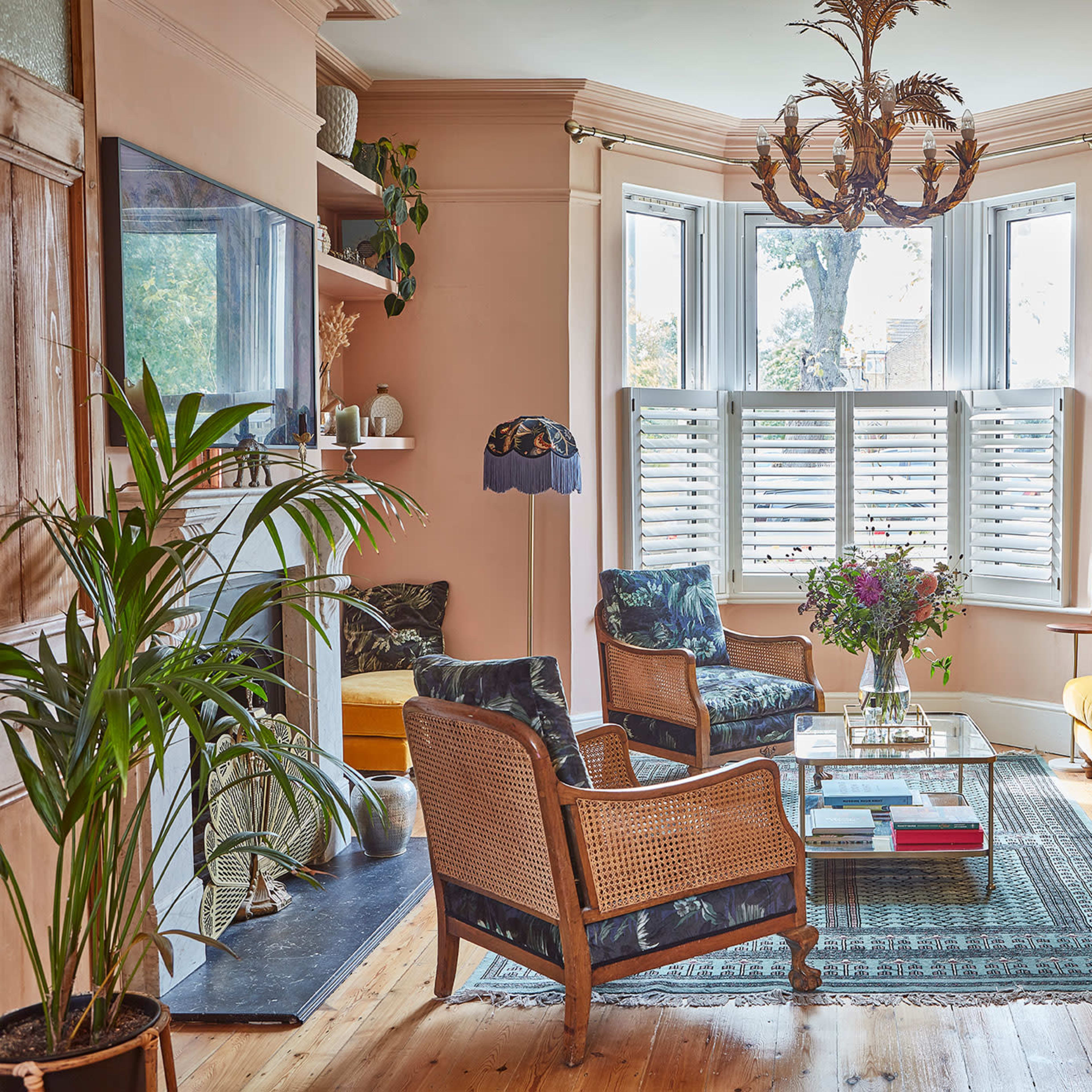A brightly lit living room featuring a mix of seating options, including a yellow sofa, an armchair, and a coffee table surrounded by plants and natural light from large windows.