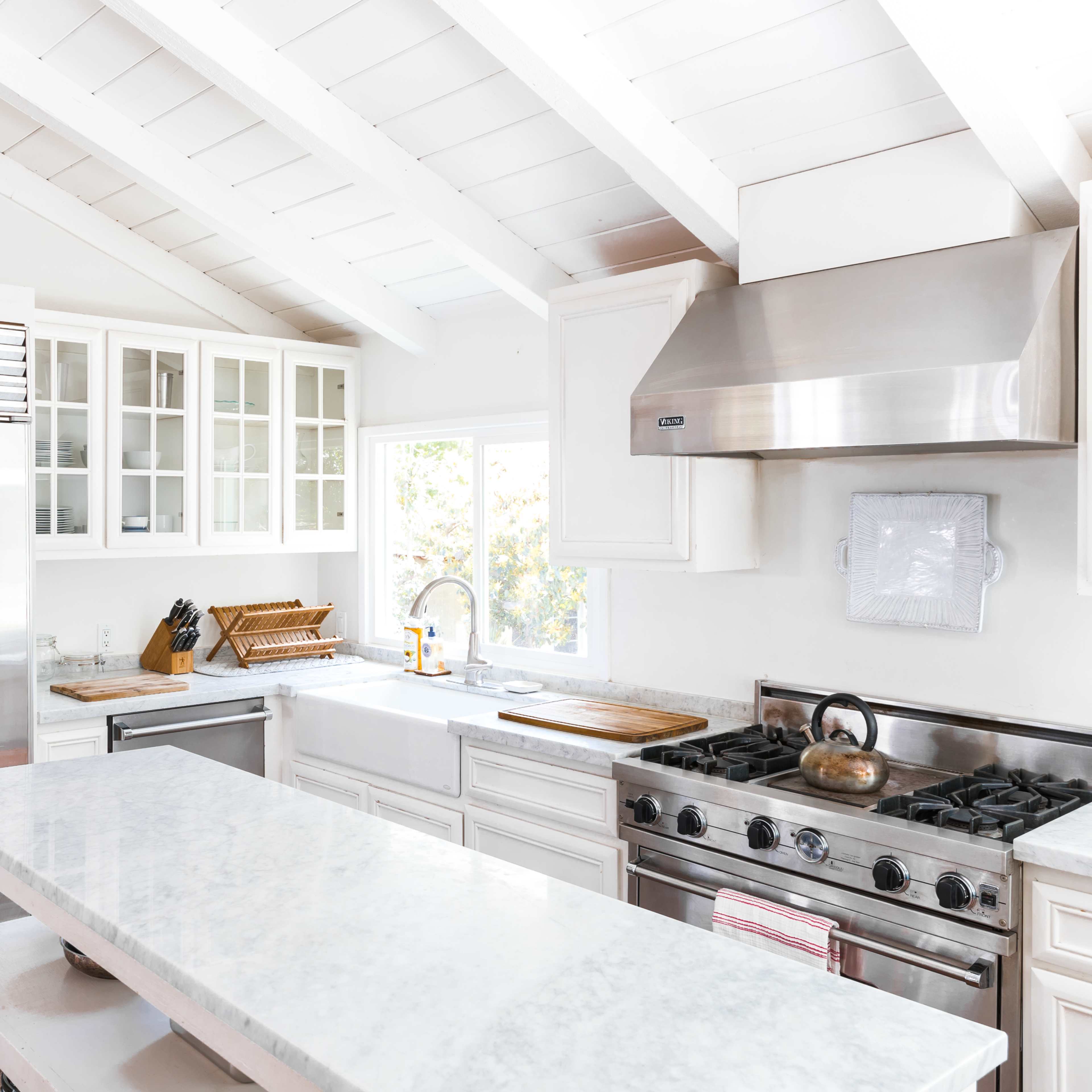 The kitchen features a stainless steel refrigerator, a gas stove, and white cabinetry with a marble island countertop.
