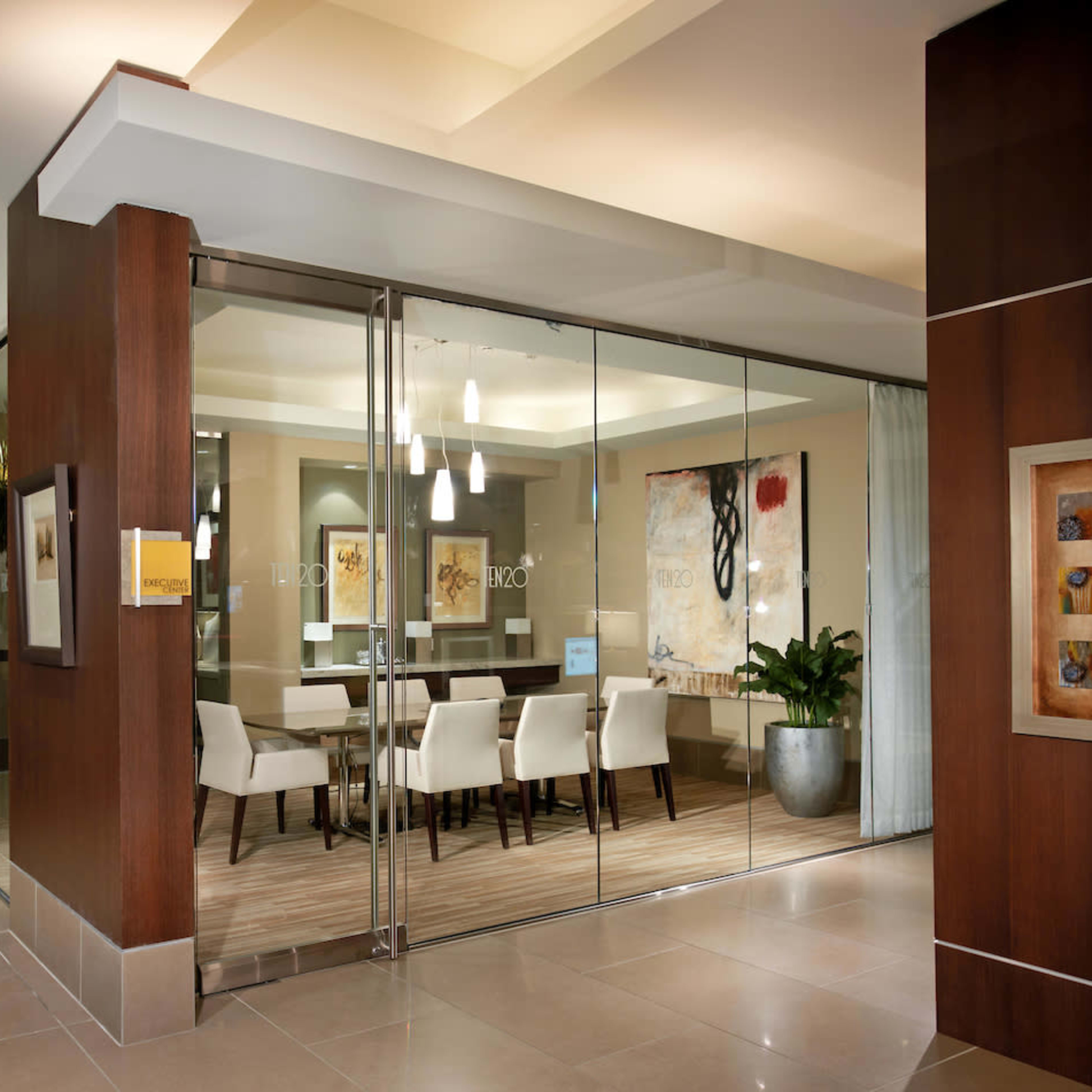 A modern conference room is visible through a glass-walled enclosure, featuring a long table and several chairs in a well-lit space with contemporary decorations.