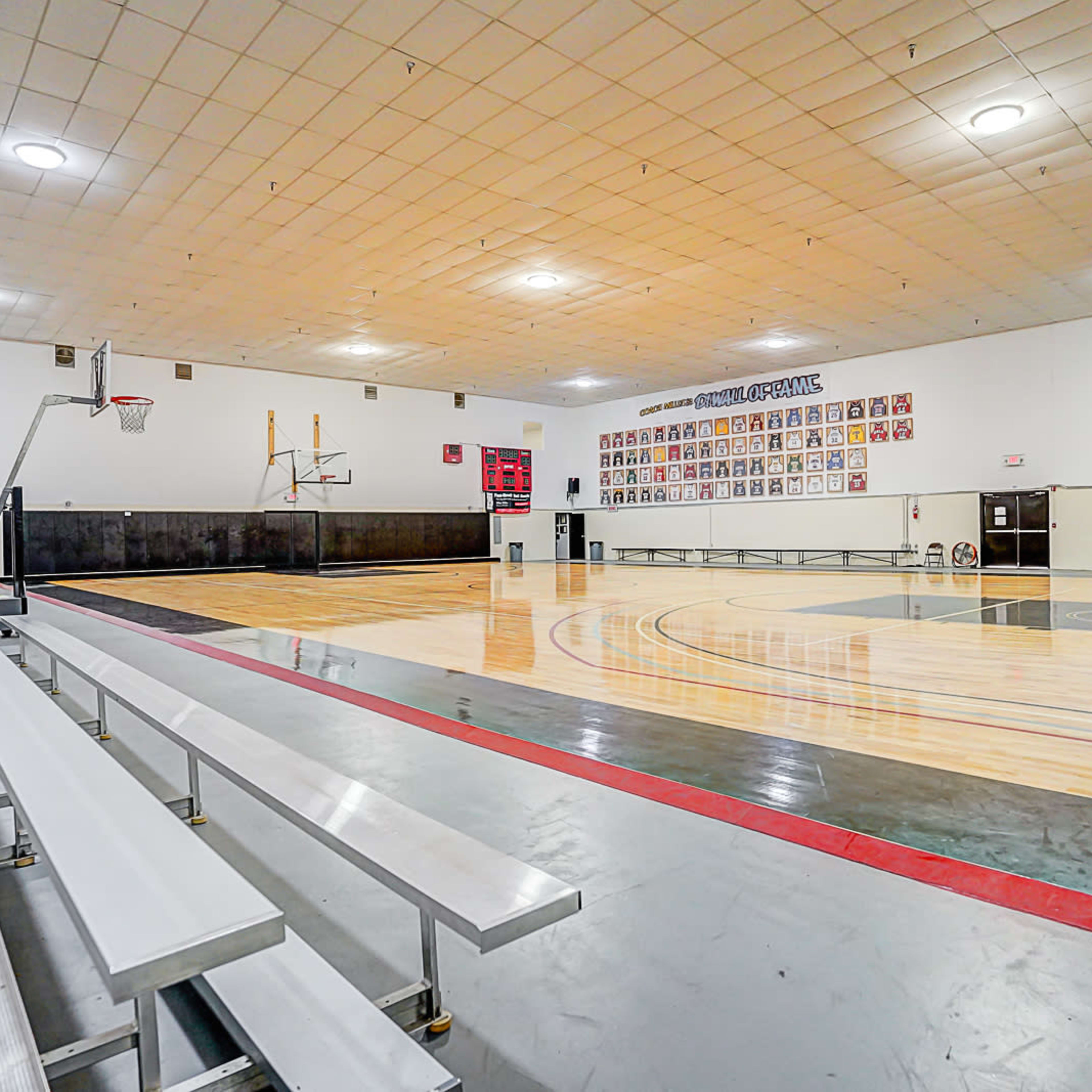 An empty basketball gymnasium with bleachers, multiple basketball hoops, and a polished wooden court.