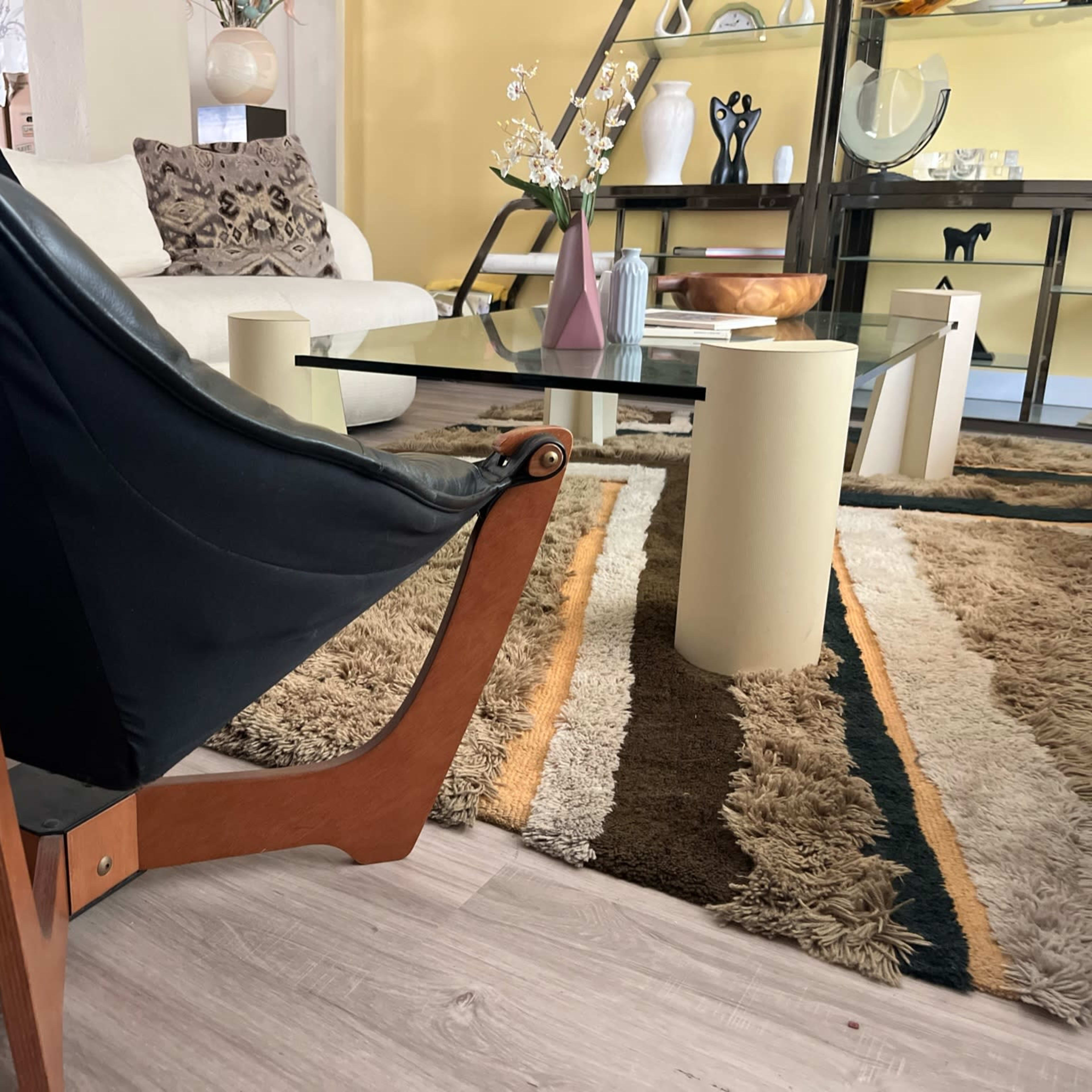 A modern living room with a black chair, a glass coffee table, and a patterned rug.