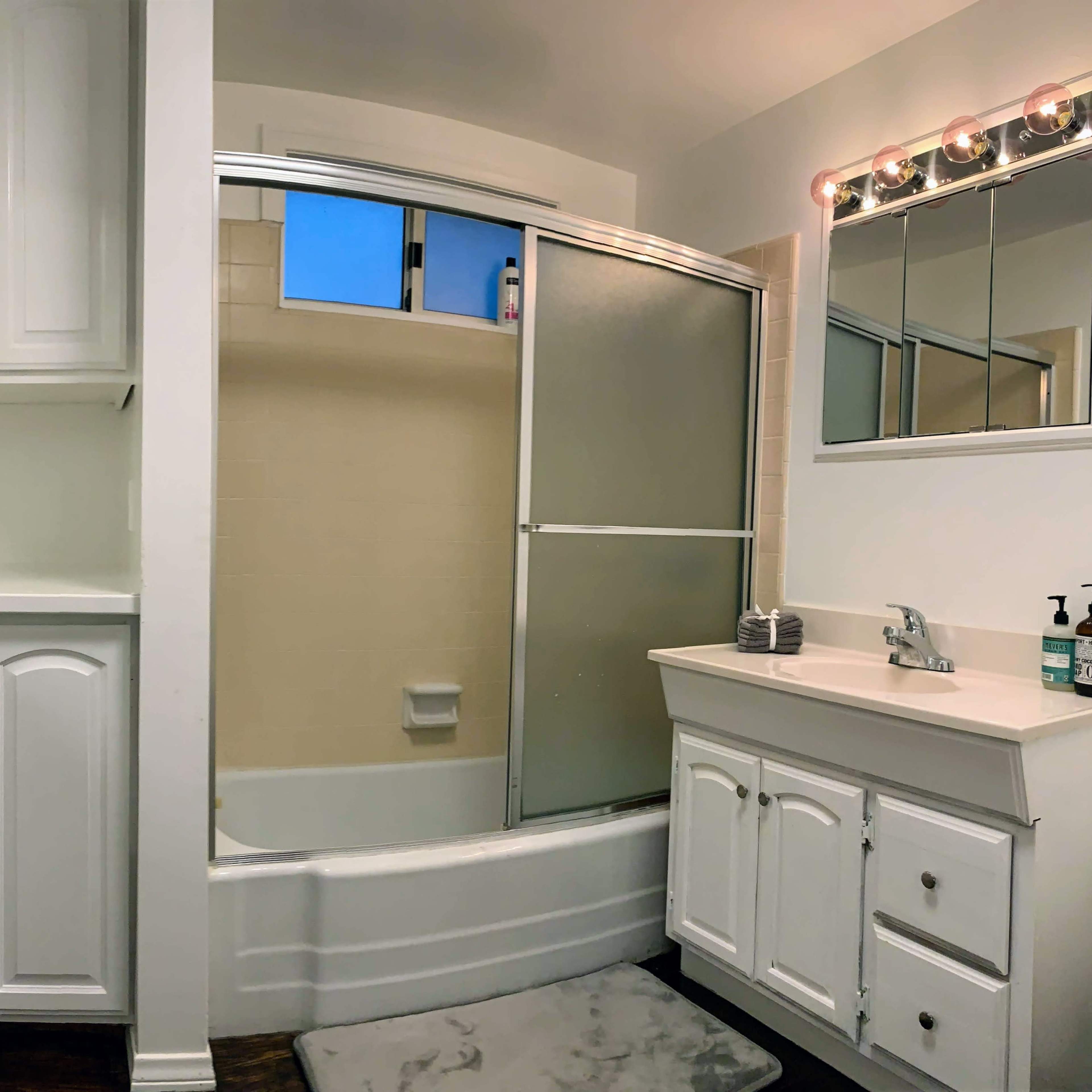 A compact bathroom featuring a shower with a sliding glass door, a sink with a cabinet beneath, and white cabinetry on the walls.