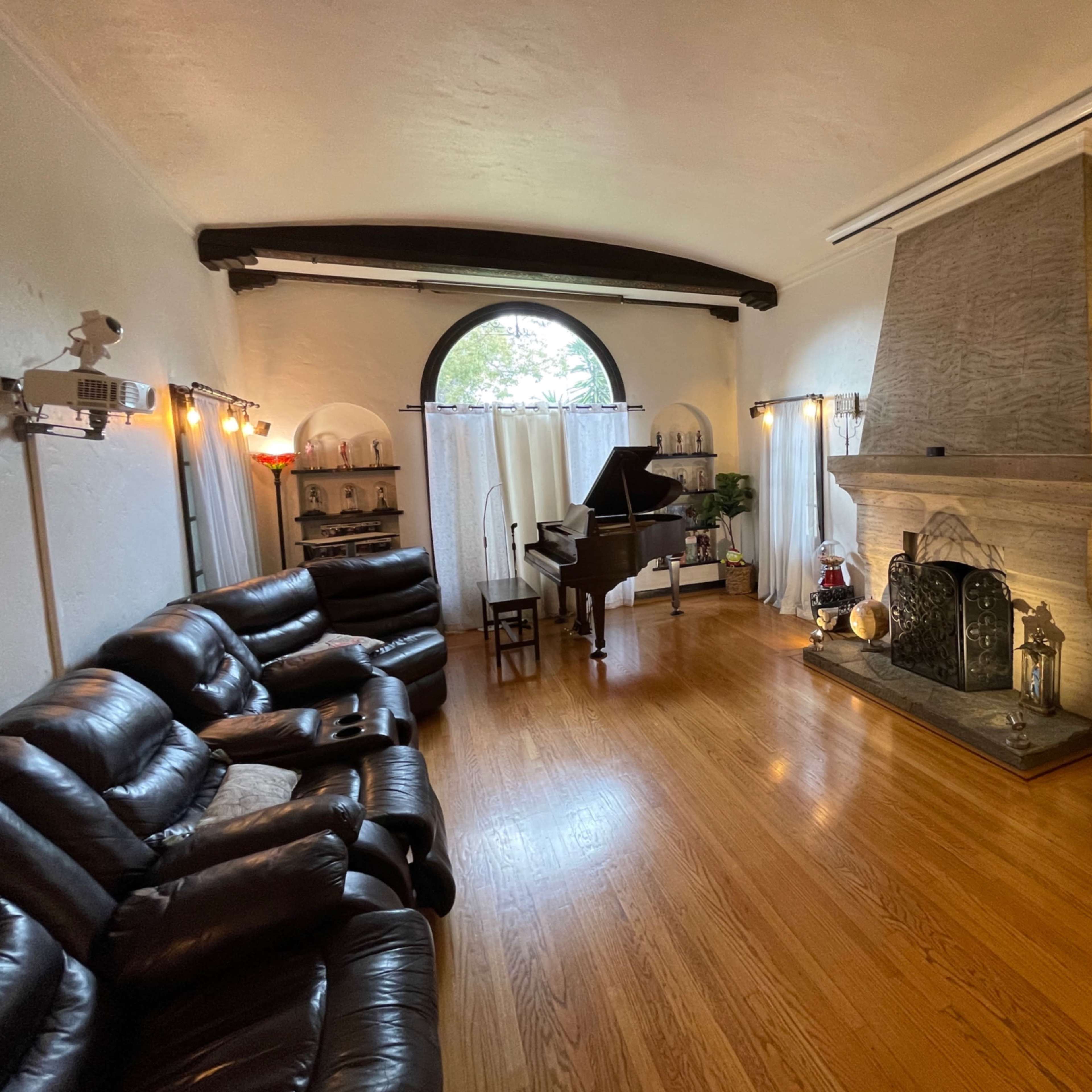 A spacious living room with a grand piano near a stone fireplace and a seating area filled with black leather couches.