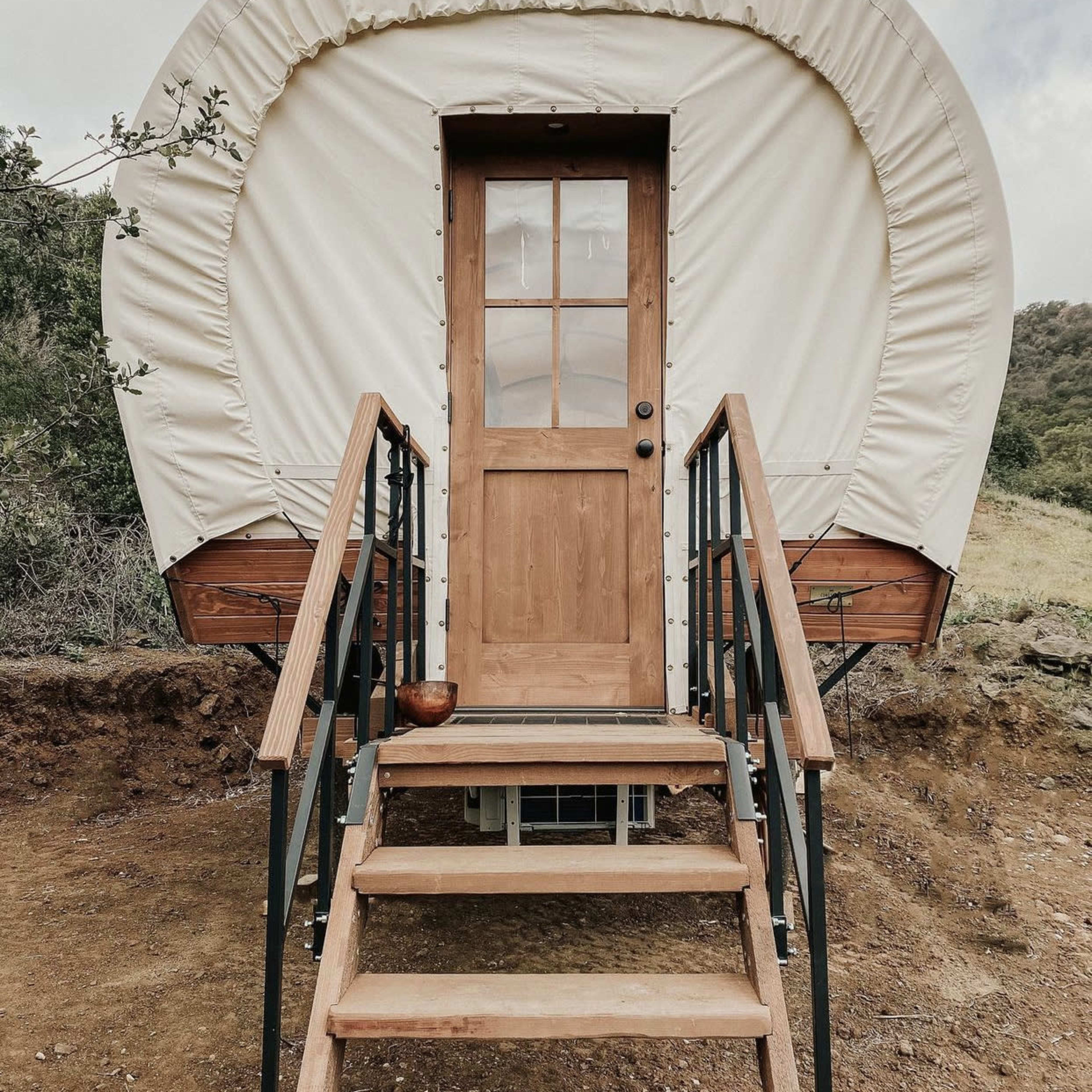 A round, canvas-covered structure with a wooden door and steps leads up to its entrance.