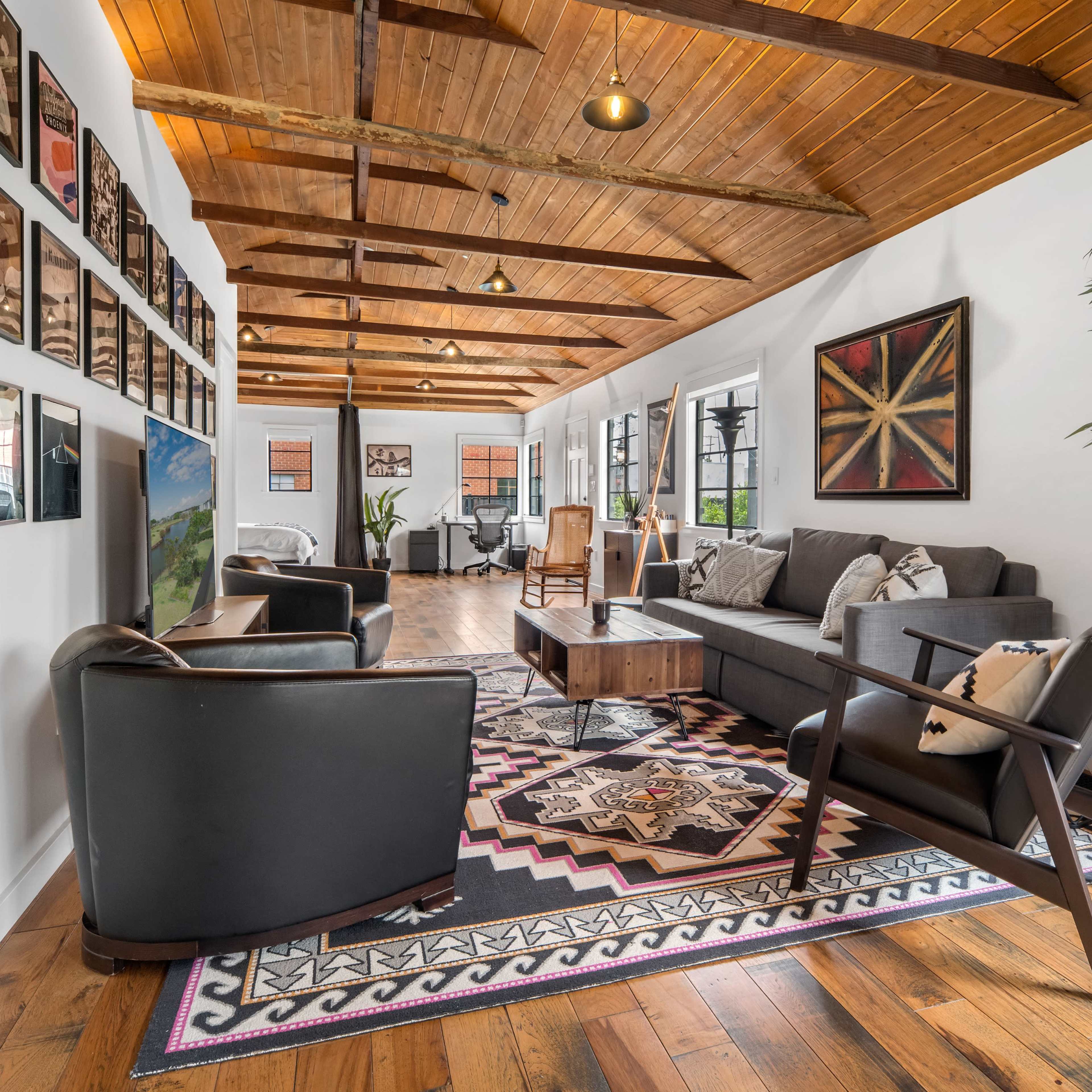 The room features a sitting area with a gray sofa, dark chairs, wooden beams, and a gallery of framed photos on the walls.