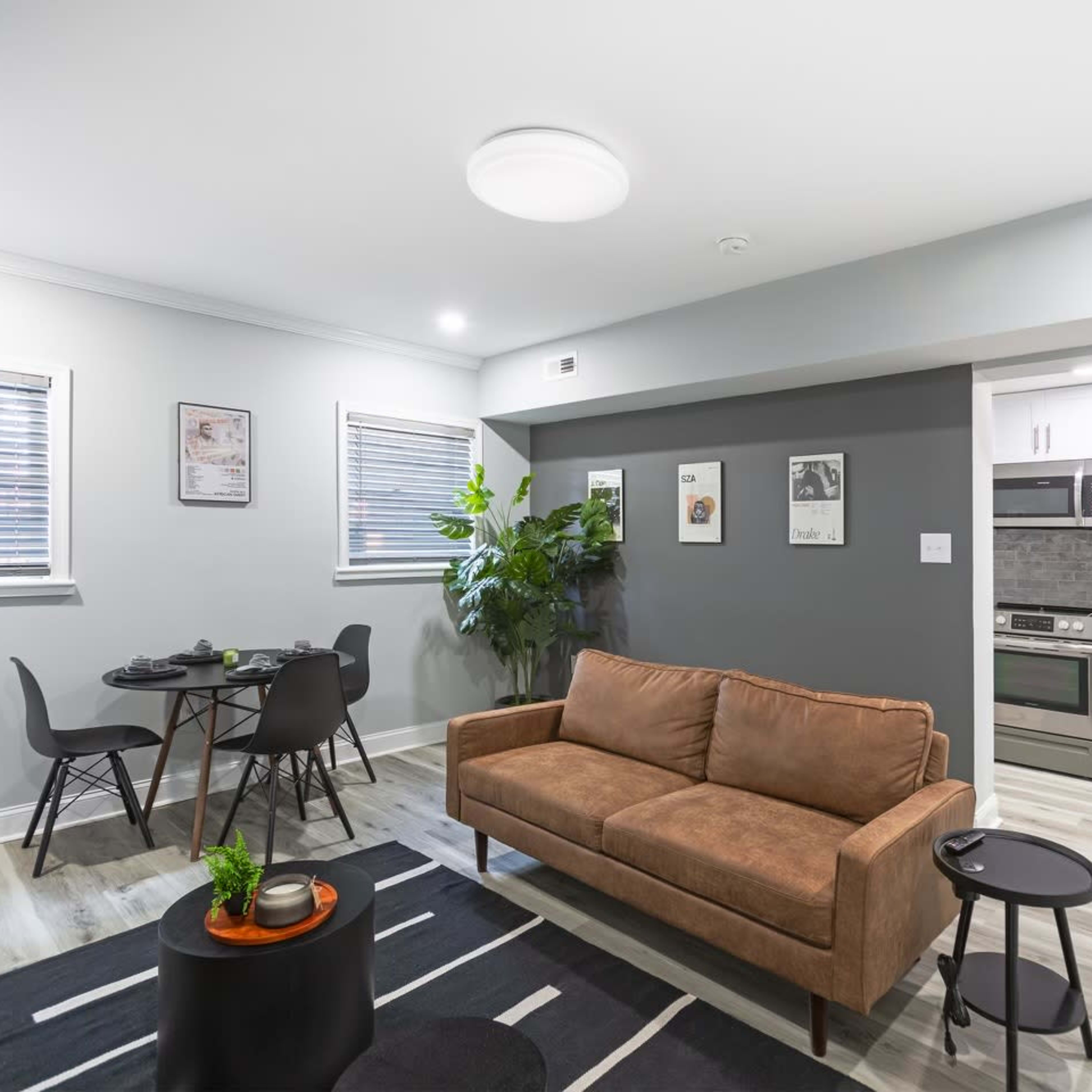 A modern living area with a brown sofa, a small round table with chairs, and a kitchen area visible in the background.