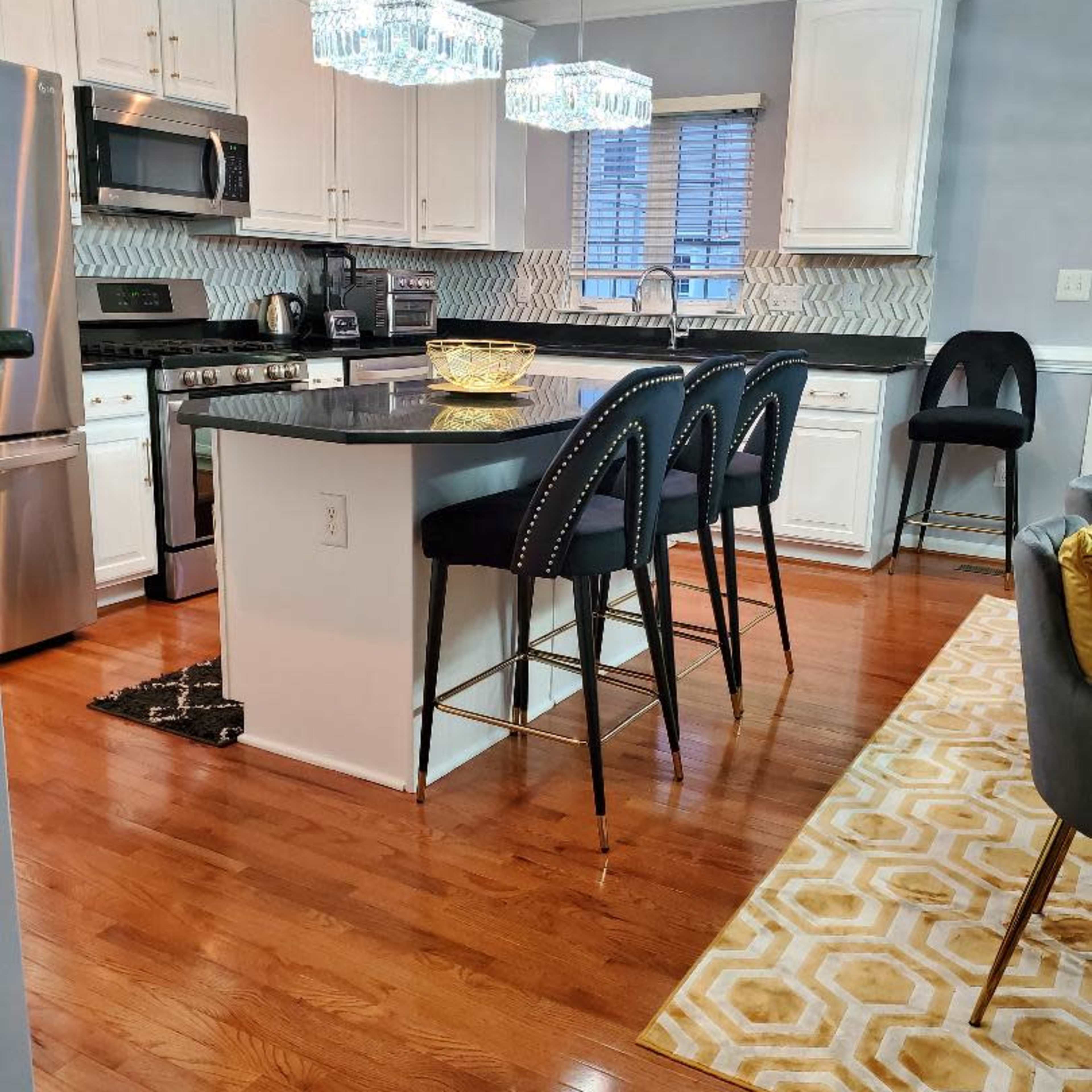 A modern kitchen features a central island with seating, stainless steel appliances, and decorative light fixtures above.