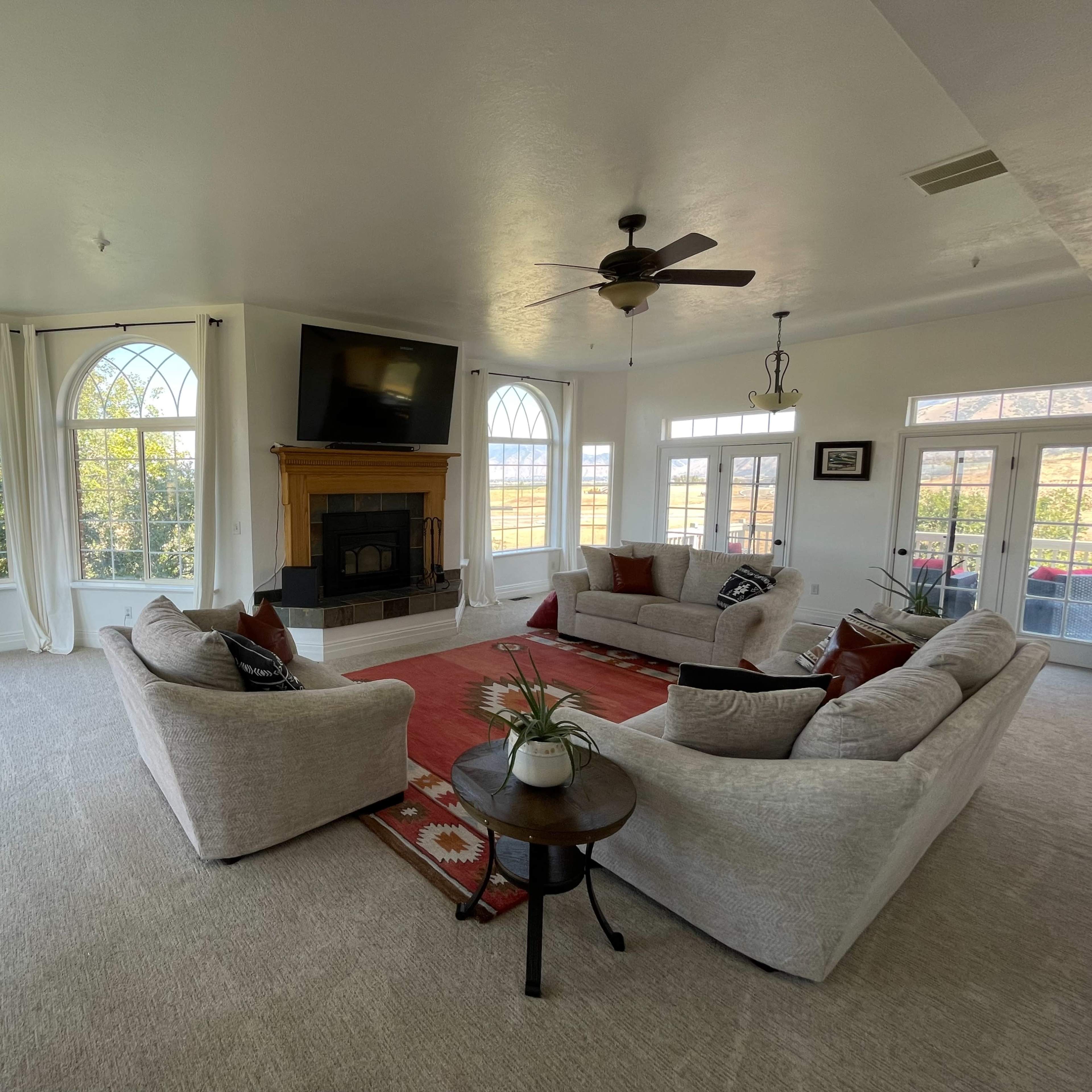 A spacious living room featuring two large sofas, a fireplace with a television above it, and large windows letting in natural light.