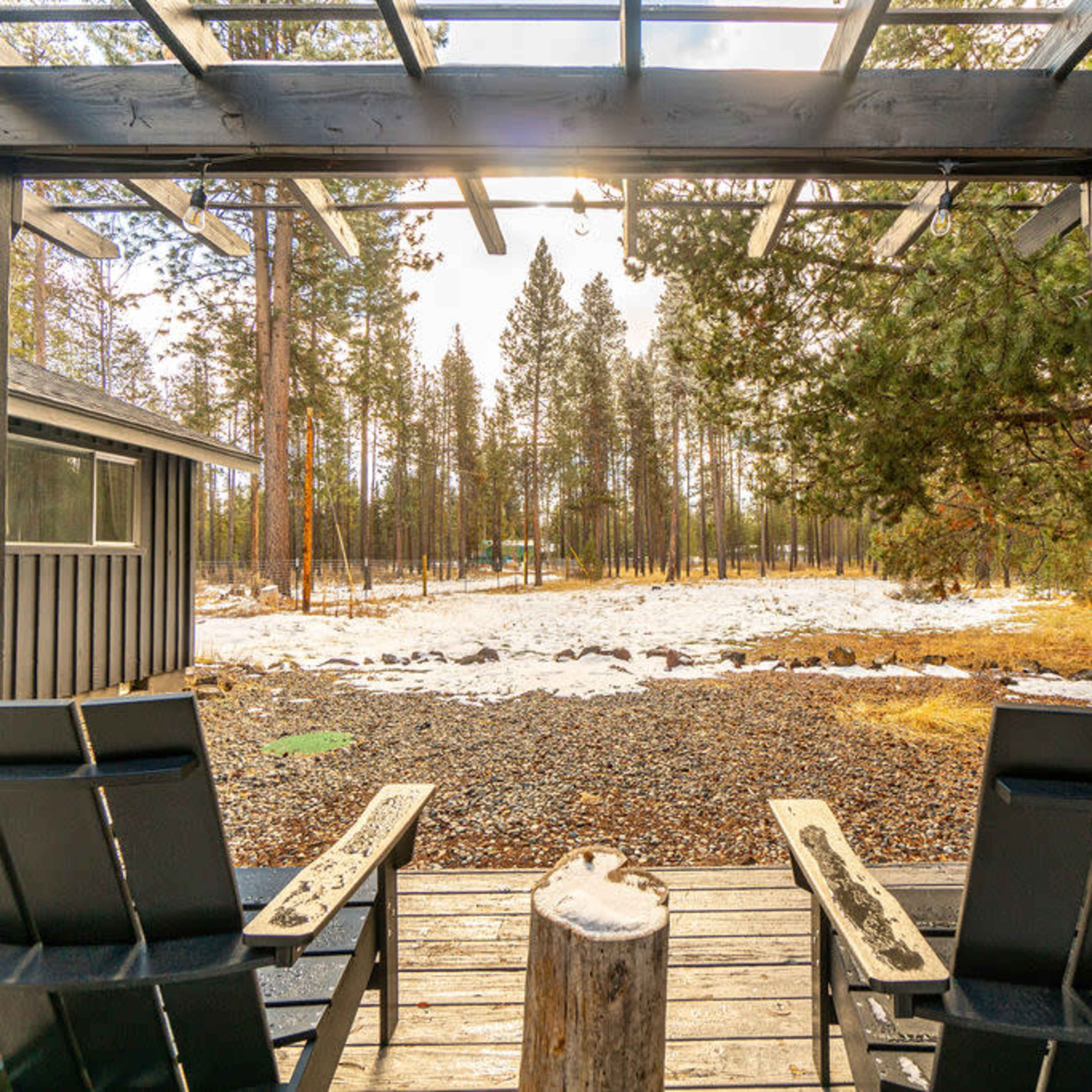 Two adirondack chairs sit on a wooden deck overlooking a snowy and wooded landscape.