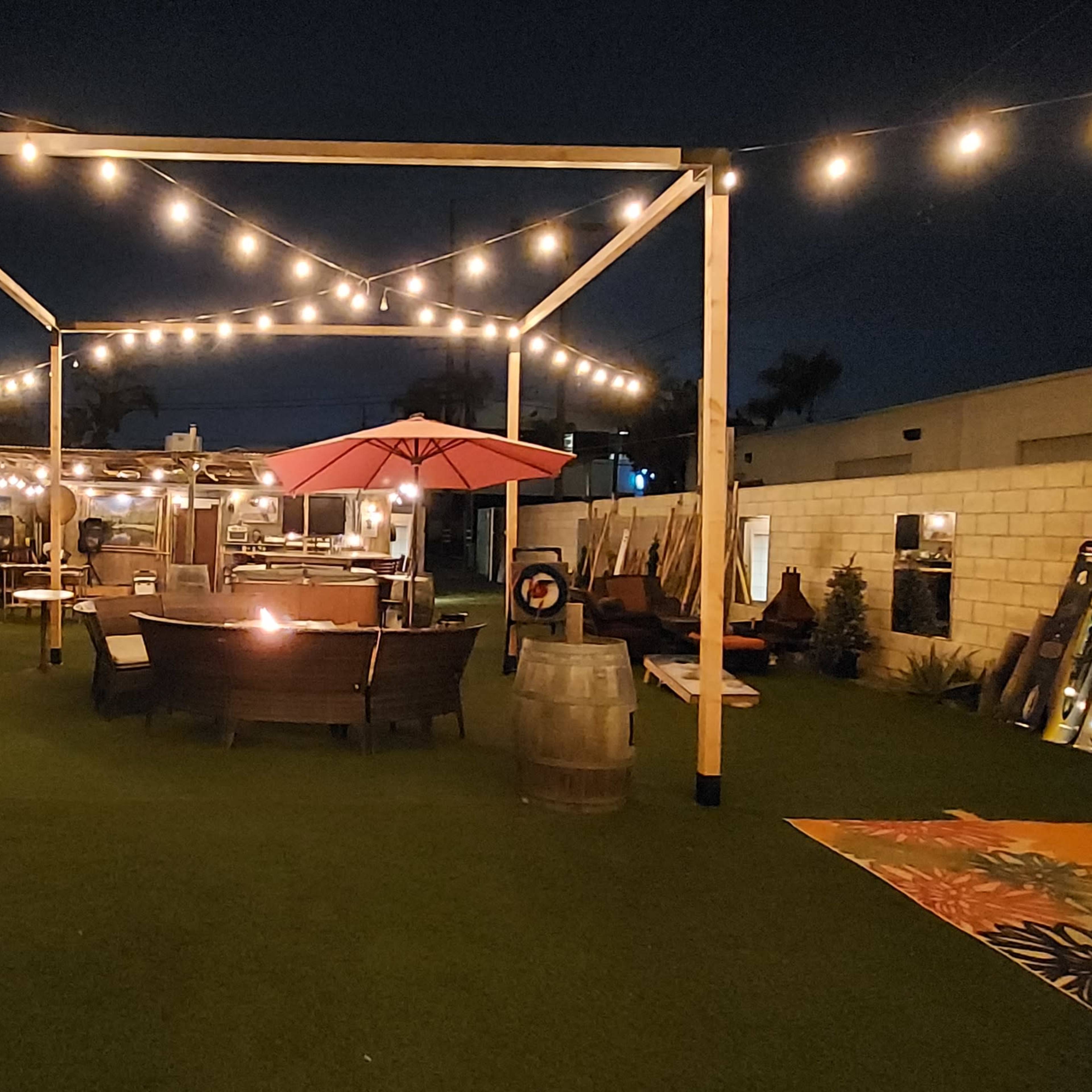 A dimly lit outdoor patio area with string lights, a ping pong table, seating arrangements, and a large umbrella.