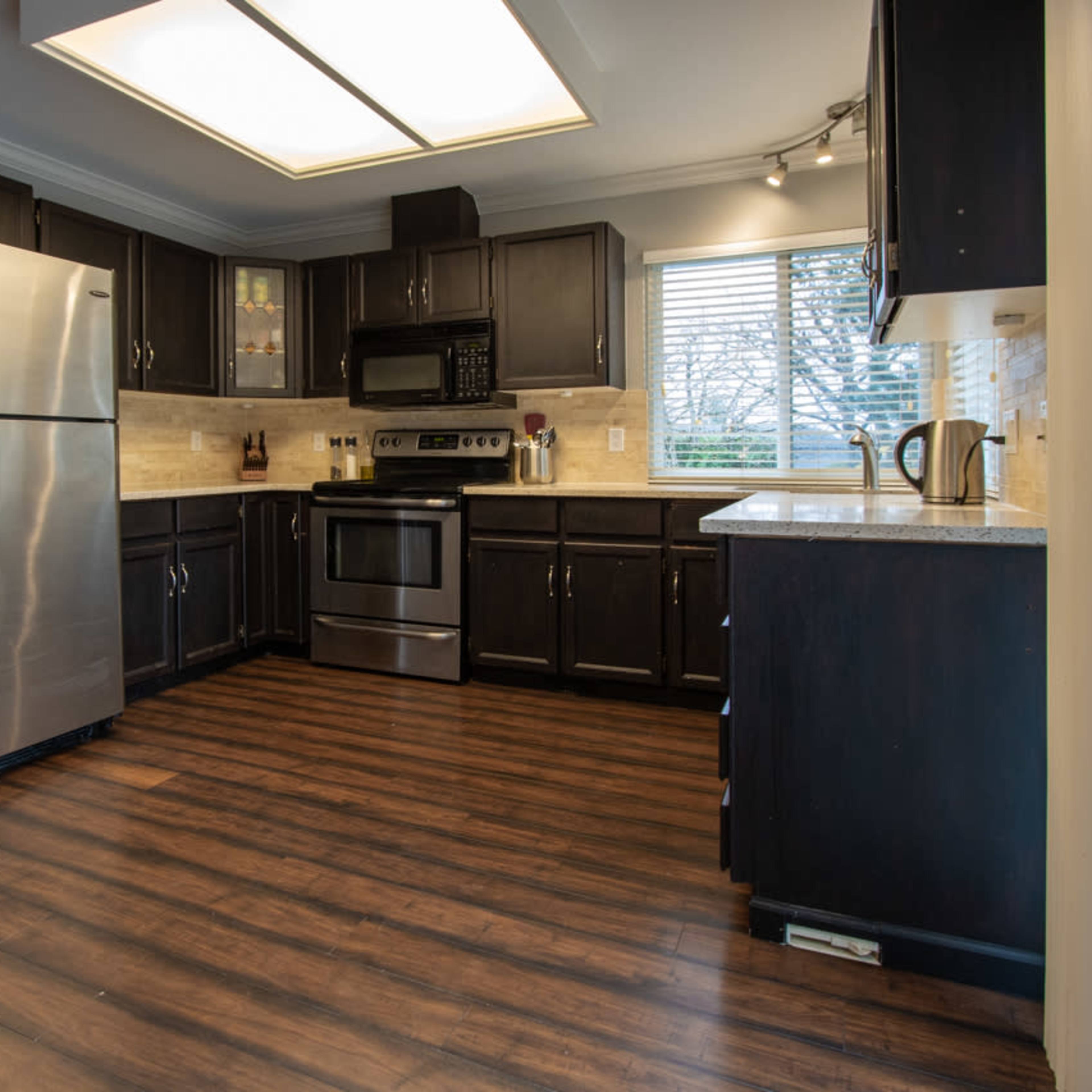 The kitchen features dark cabinetry, a stainless steel refrigerator, an oven, and a window with blinds.