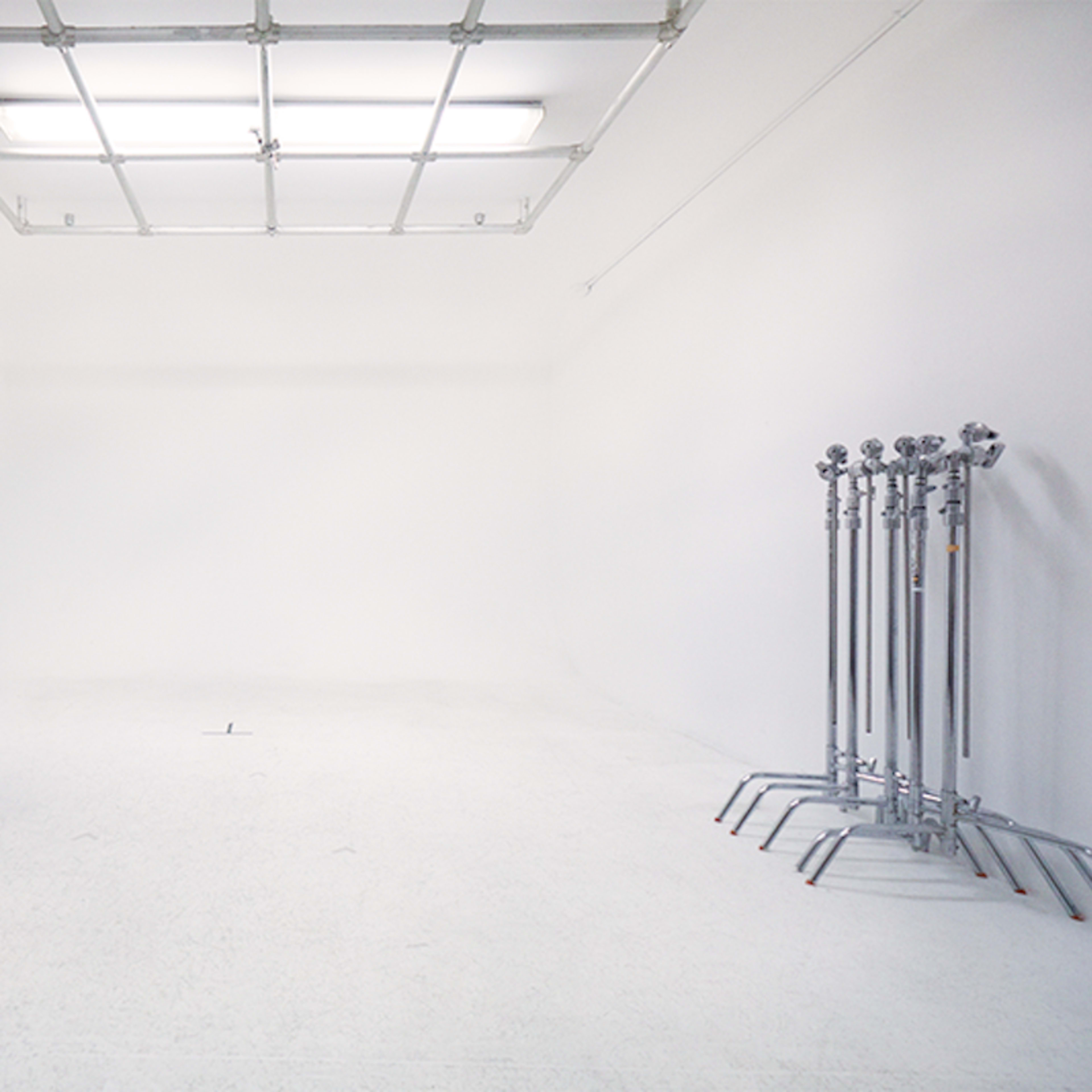 A minimalist studio space with a large white wall, a desk with drawers on one side, and several tripod stands lined up against another wall.
