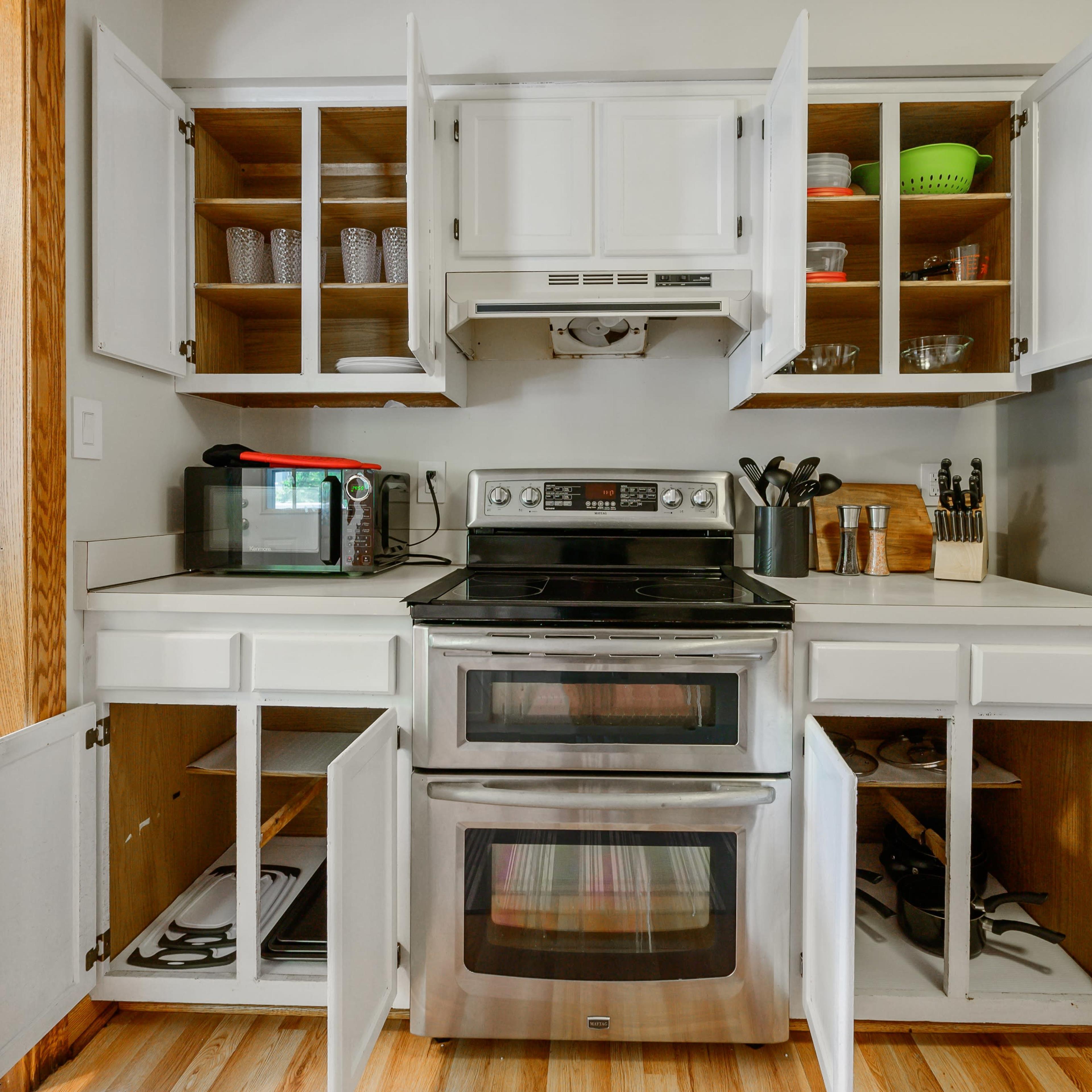 A kitchen with an oven, a microwave, and open cabinets displaying dishware and kitchen utensils.