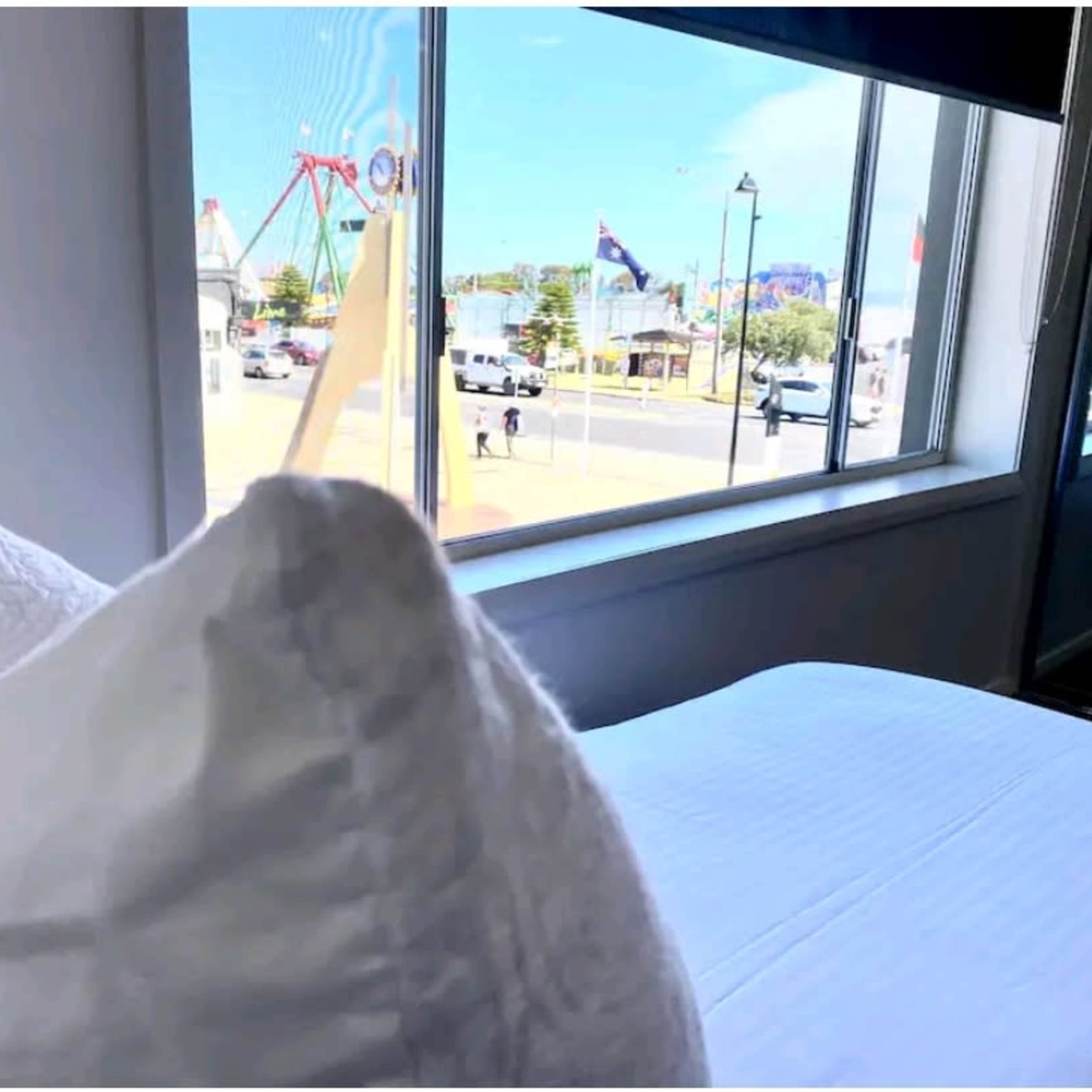 A white pillow is placed on a bed in front of a window showing a colorful amusement park in the distance.