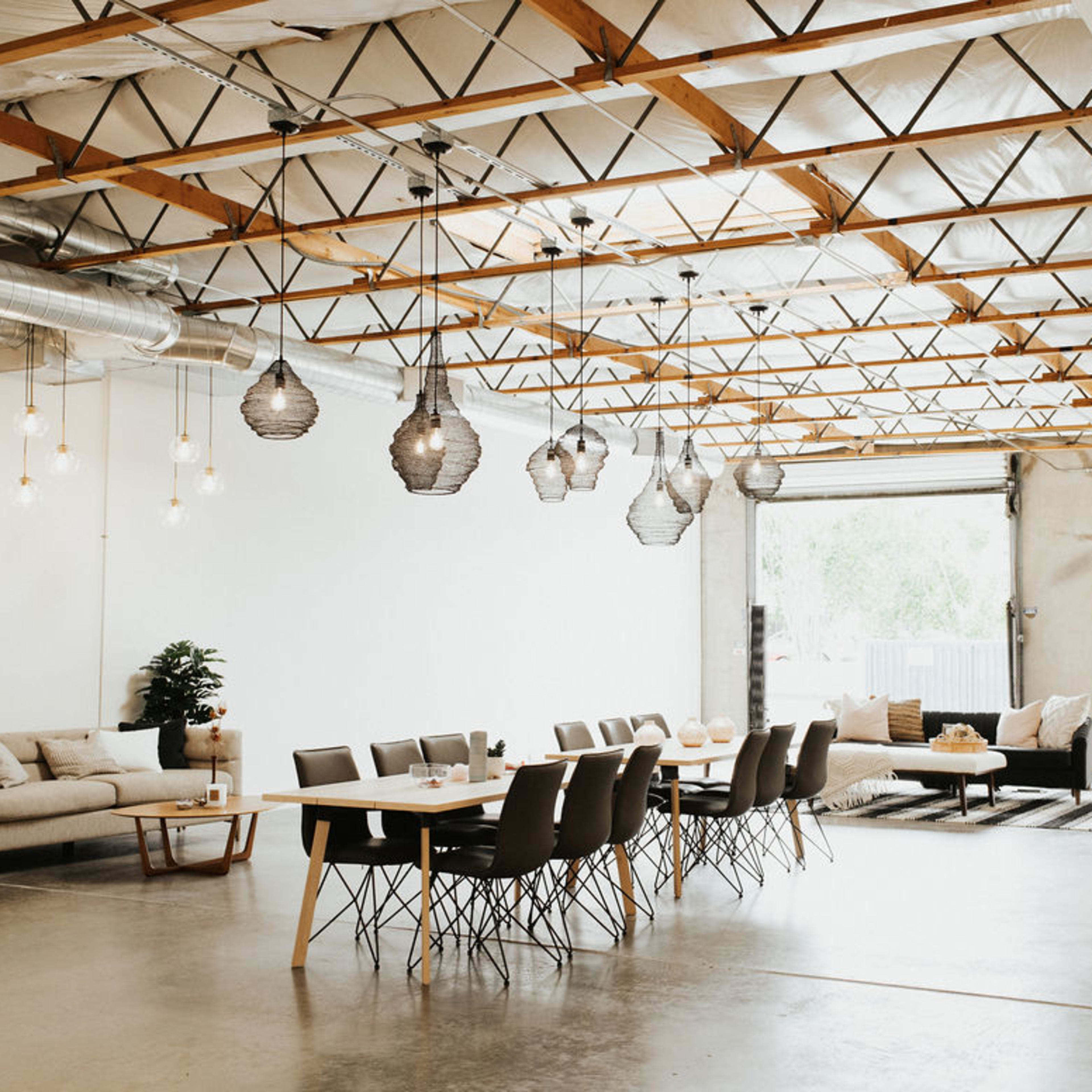 A spacious interior with a dining table surrounded by chairs, a sofa, and hanging light fixtures under a vaulted ceiling.
