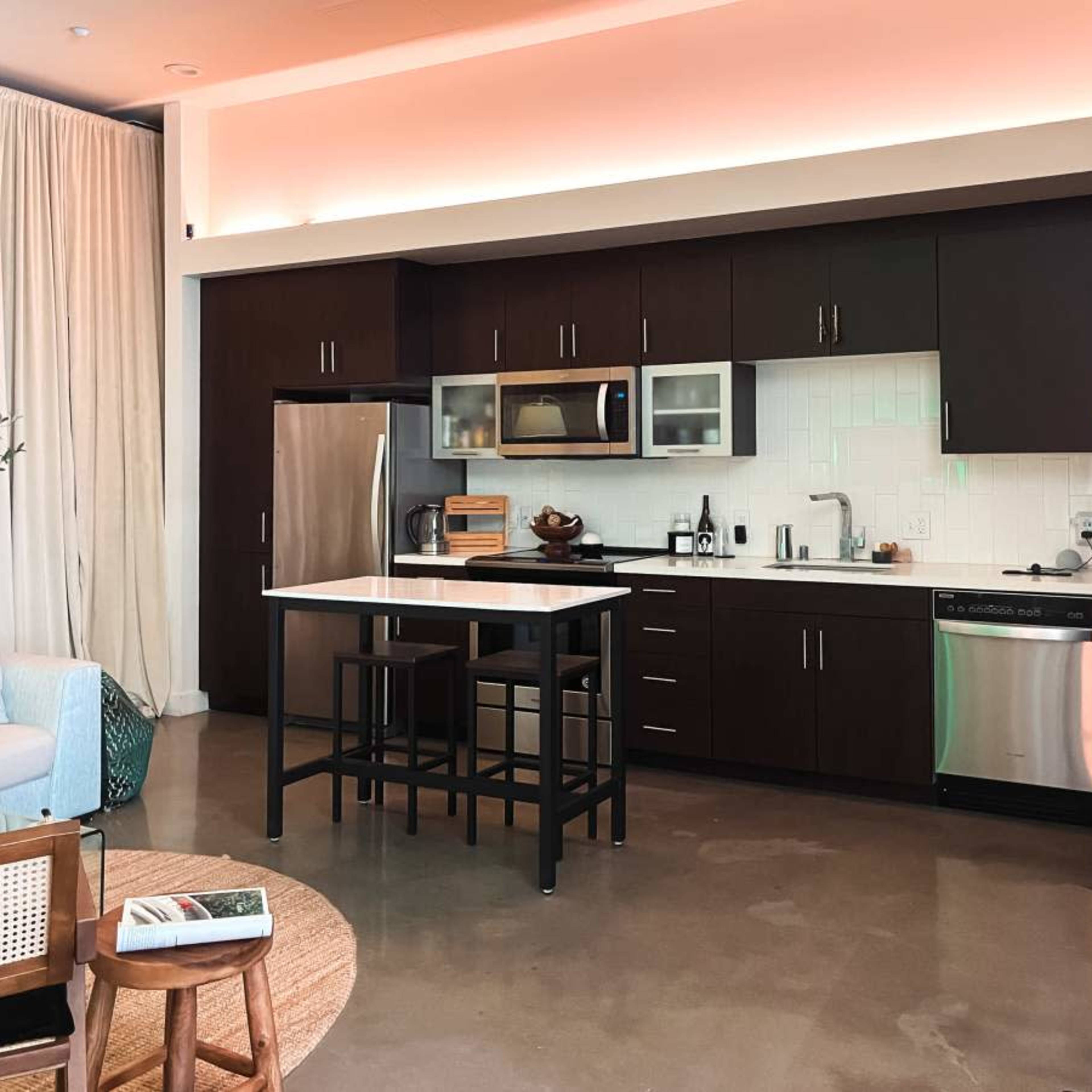 A modern kitchen with dark cabinets, stainless steel appliances, and a central island, accompanied by a seating area.