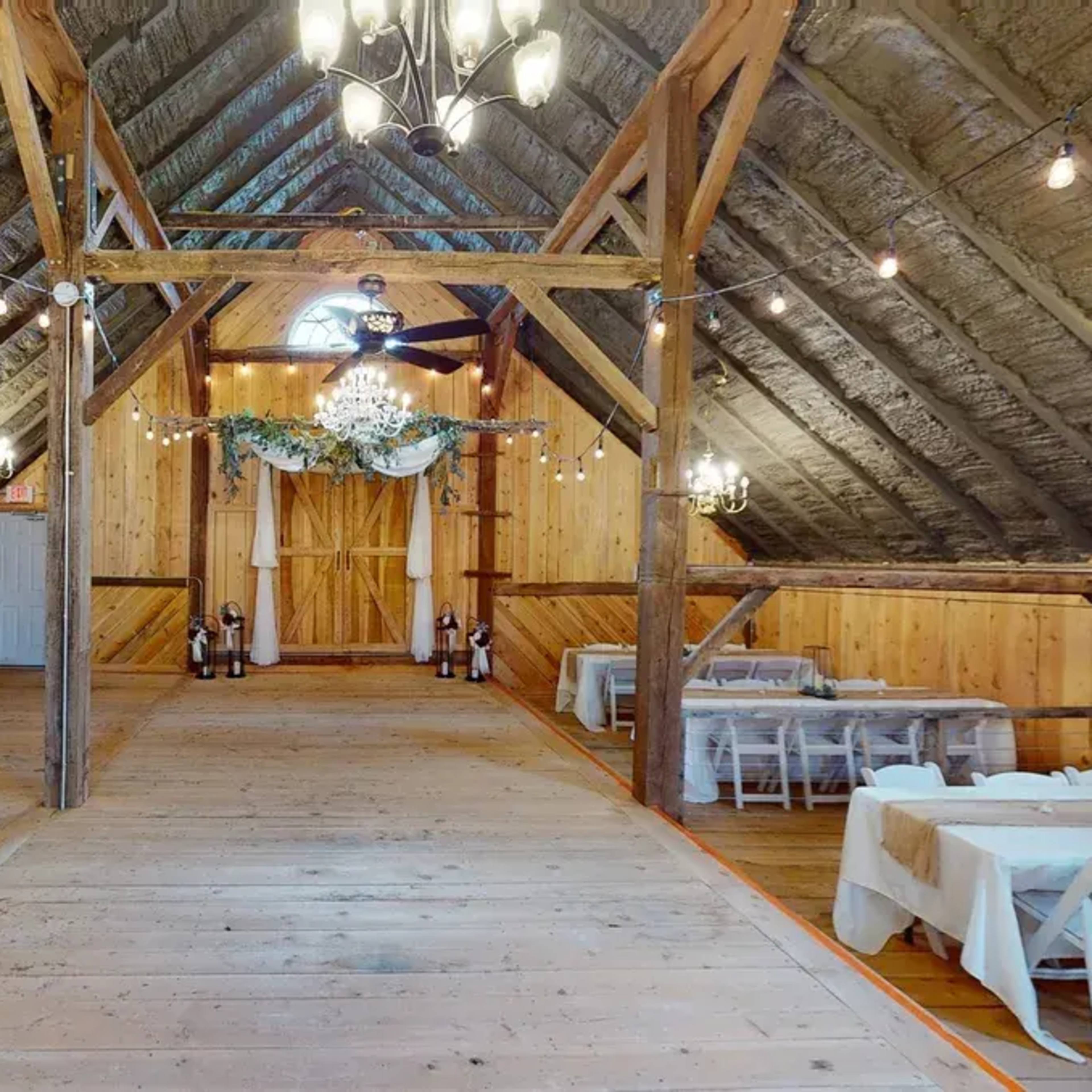 The interior of a rustic barn venue with wooden walls, a wooden floor, and tables arranged for an event.